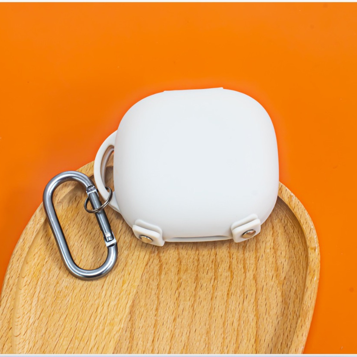 Weißes Ohrhörer-Etui mit silbernem Karabinerhaken auf einem Holztablett, vor orangefarbenem Hintergrund.