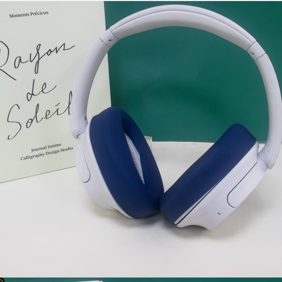 Cuffie bianche con padiglioni auricolari blu scuro sono mostrate accanto a un libro su una superficie bianca.