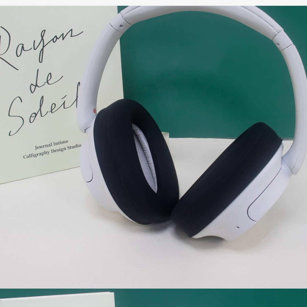 Cuscinetti auricolari neri su cuffie bianche sono mostrati accanto a un libro su una superficie bianca.
