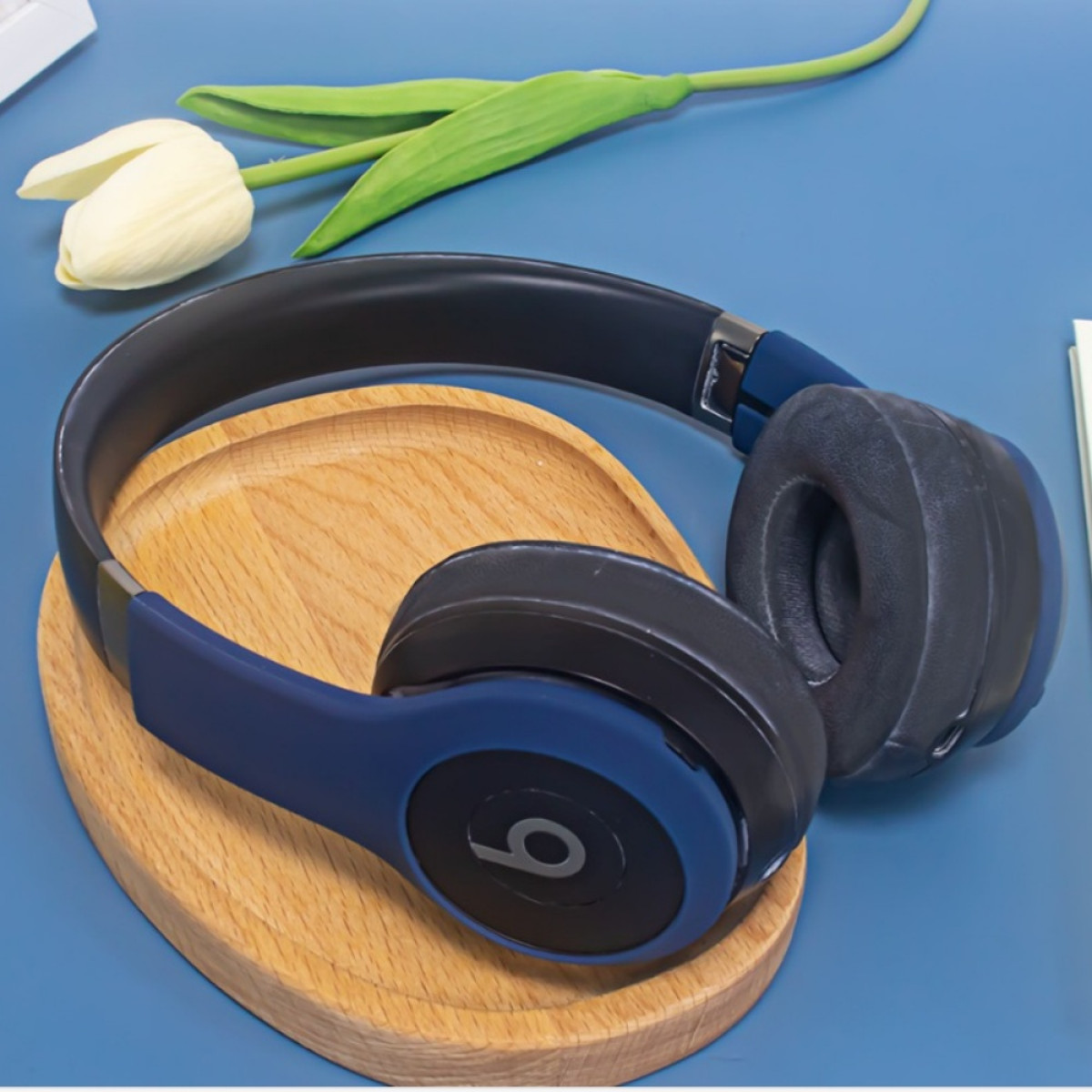 Blaue und schwarze Beats-Kopfhörer liegen auf einem Holztablett mit einer weißen Tulpe in der Nähe.