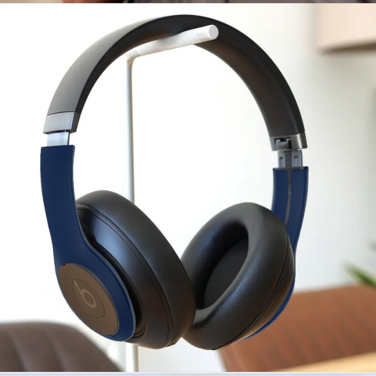 Blaue und schwarze Beats-Kopfhörer hängen auf einem weißen Ständer, mit einem verschwommenen Hintergrund.