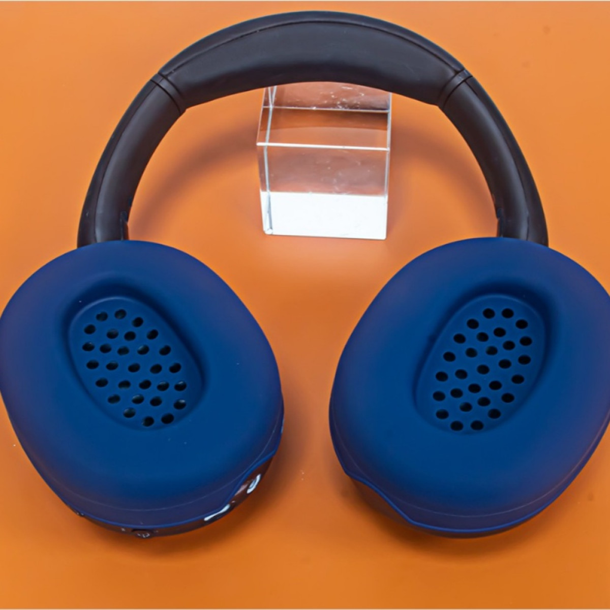 Scatto dall'alto di cuffie blu scuro con padiglioni auricolari perforati su sfondo arancione.