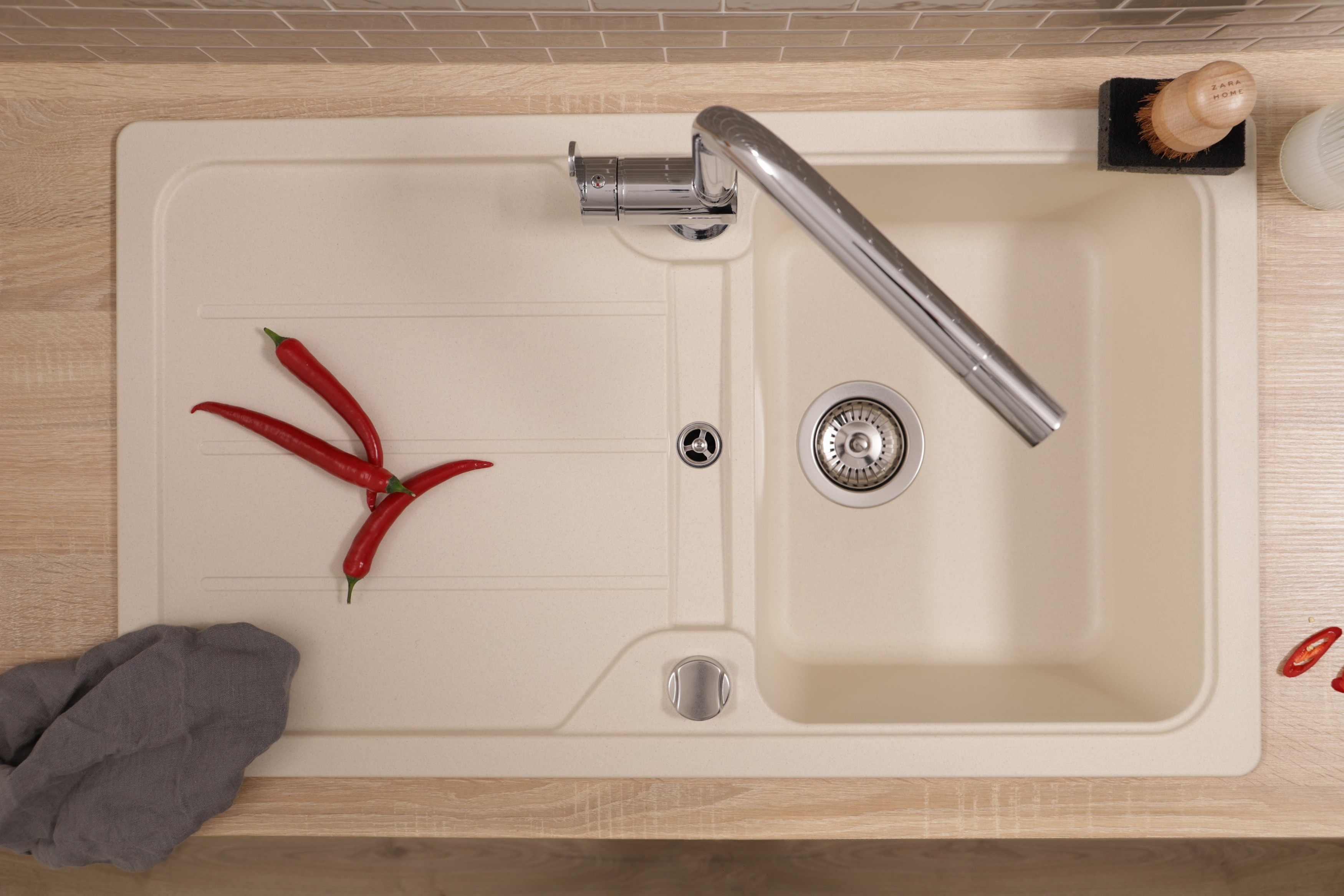 Draufsicht auf ein Küchenbecken mit Wasserhahn, roten Paprika, Holzoberfläche, und Fliesen.