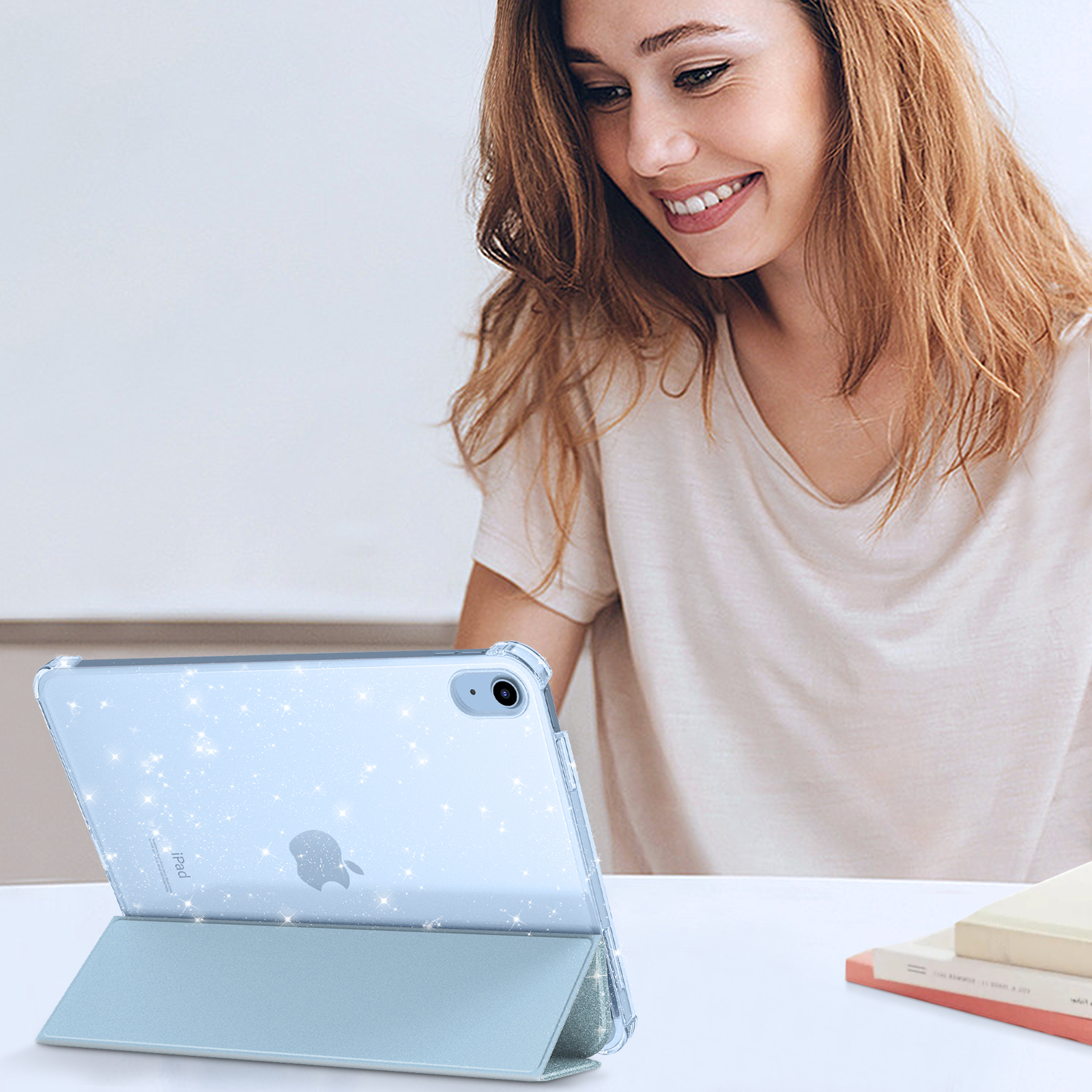 Eine Frau lächelt hinter einem hellblauen Tablet mit glitzernder Hülle auf einem weißen Tisch.