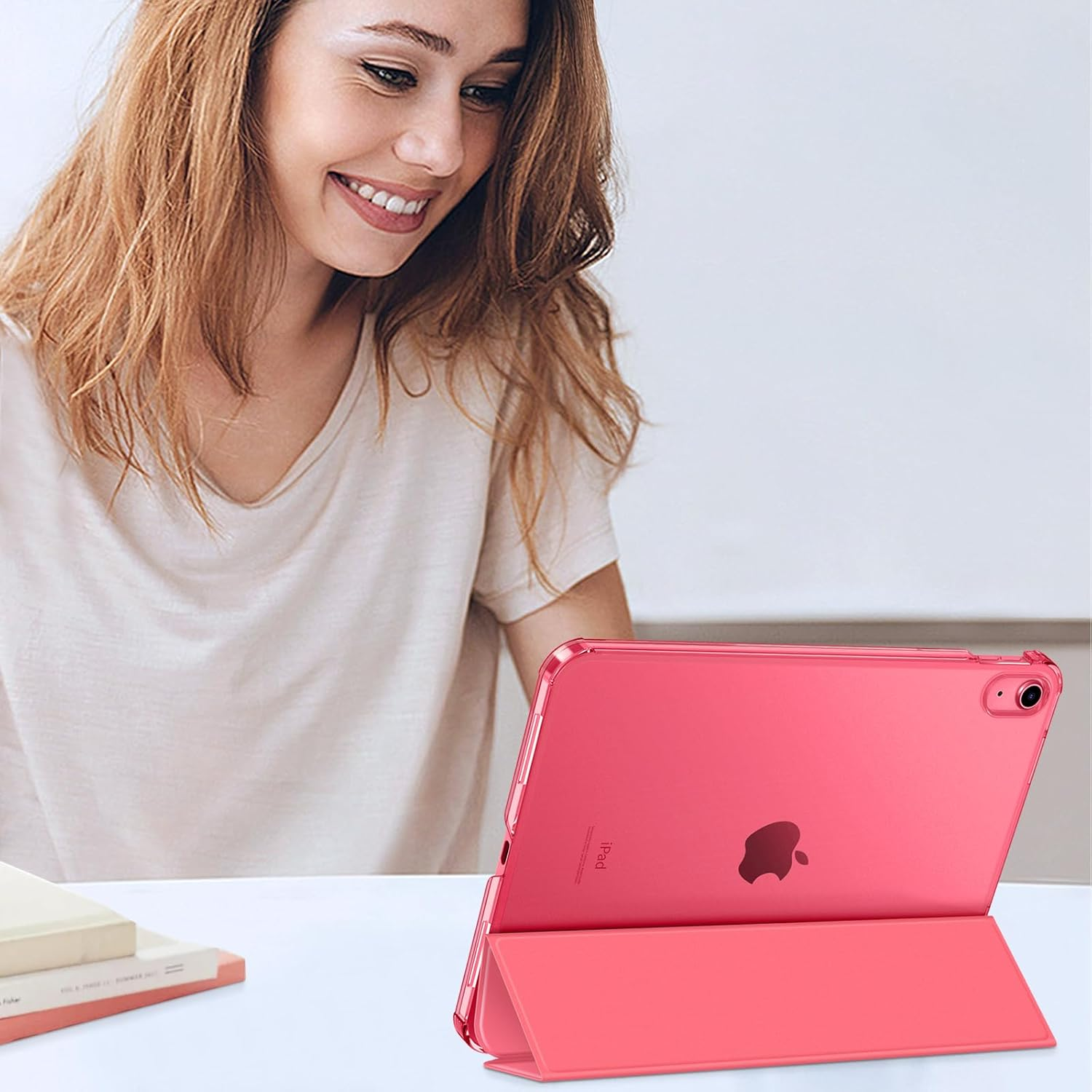 Eine Frau lächelt, während sie ein rosa iPad im Standmodus auf einem weißen Tisch benutzt.