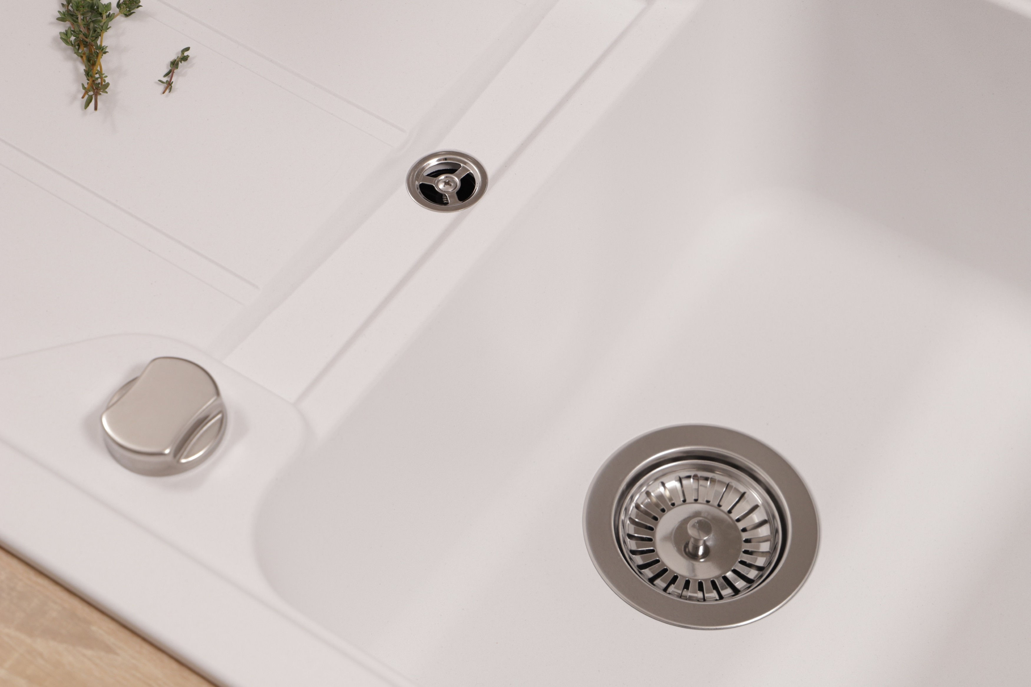 Draufsicht auf ein sauberes, weißes Spülbecken mit Abfluss, Knopf und Kräutern.