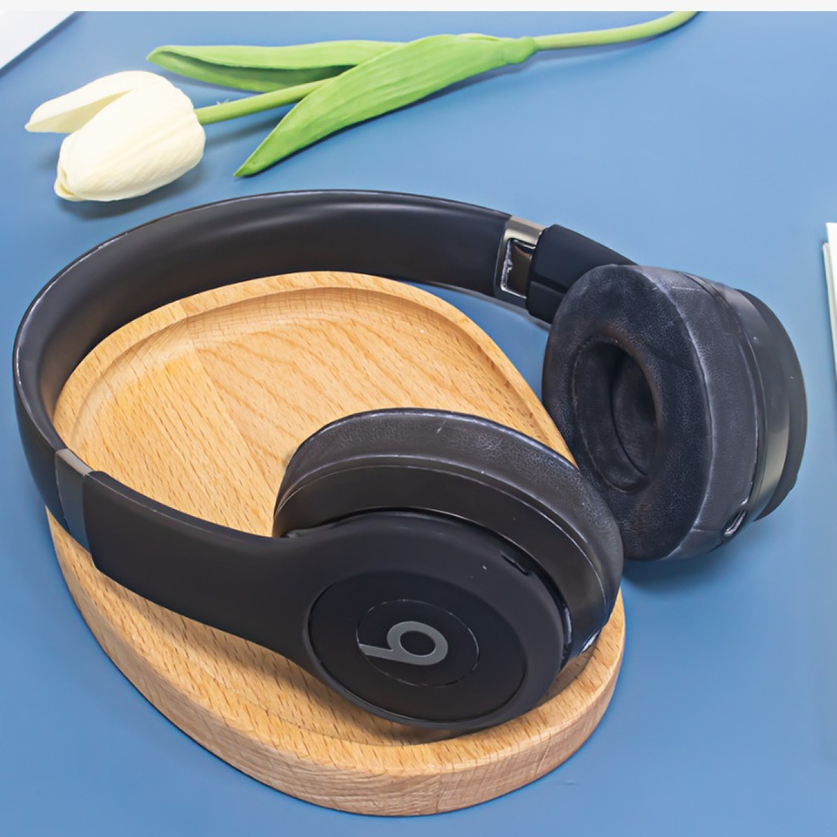 Cuffie nere su un supporto di legno, con un fiore bianco, su sfondo blu.