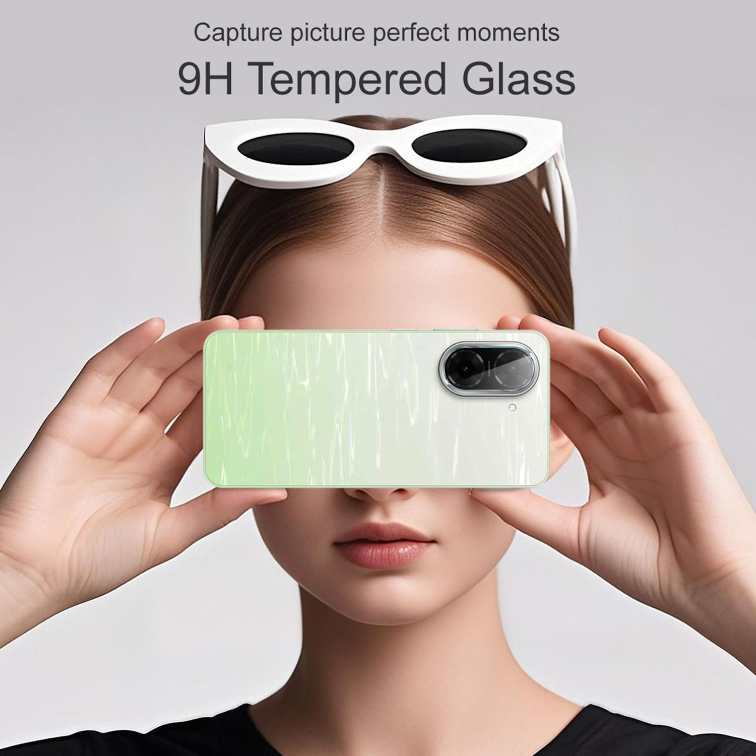 Una donna tiene un telefono verde e bianco sopra il suo viso, con occhiali da sole bianchi sulla testa.