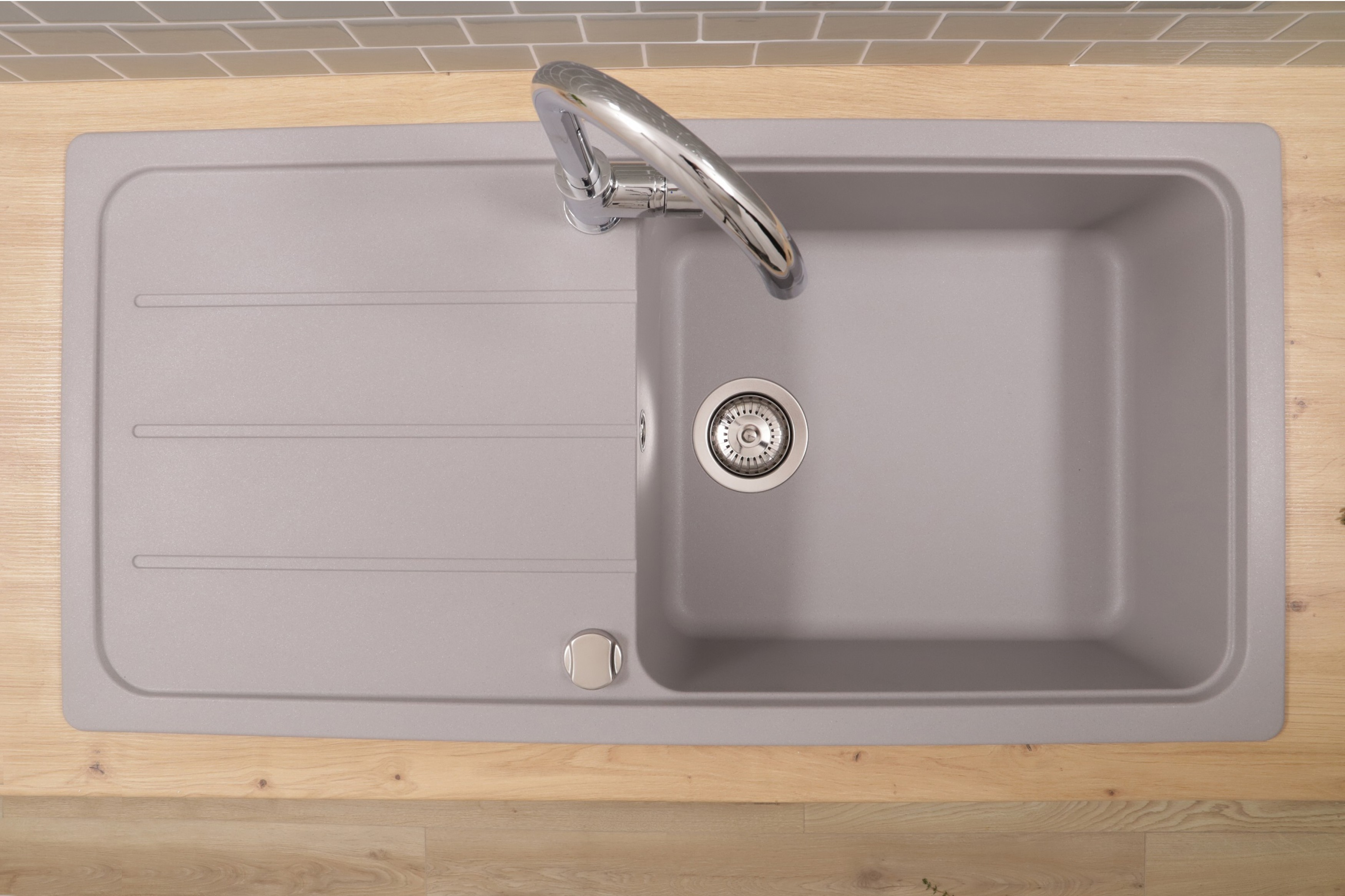 Ein graues Küchenbecken mit Wasserhahn. Das Waschbecken steht auf einer Holzplatte. Draufsicht.
