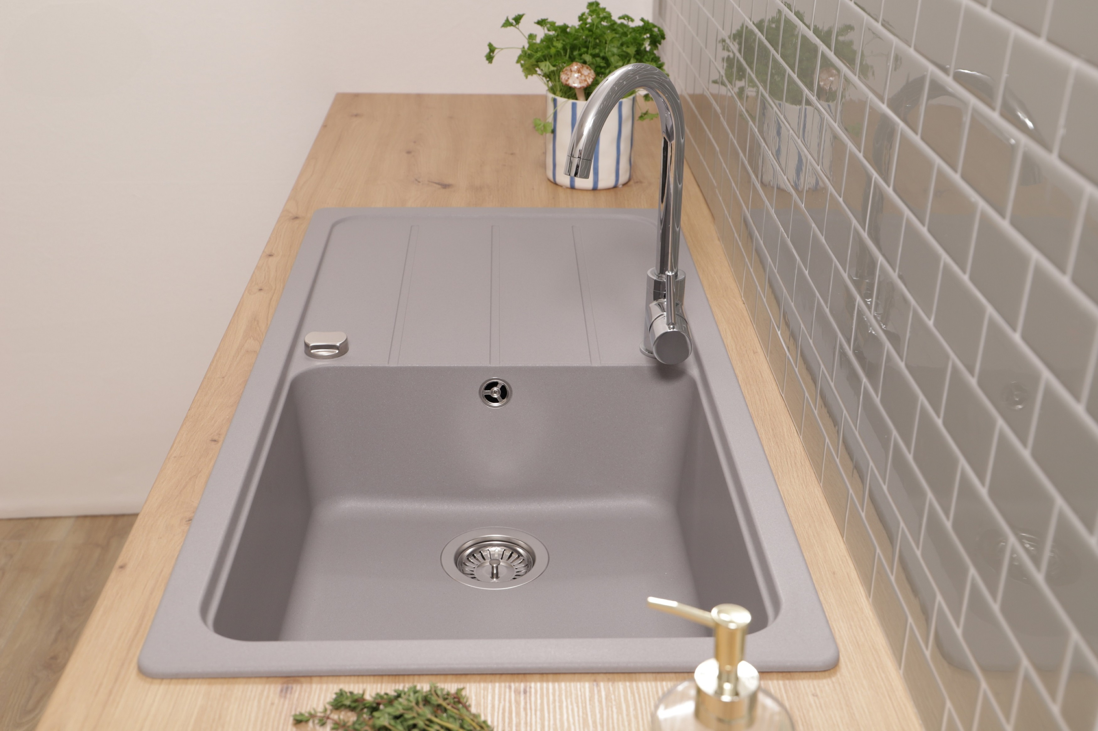 Ein graues Küchenbecken mit Wasserhahn auf einer Holzplatte. Eine Pflanze und Seife sind sichtbar.