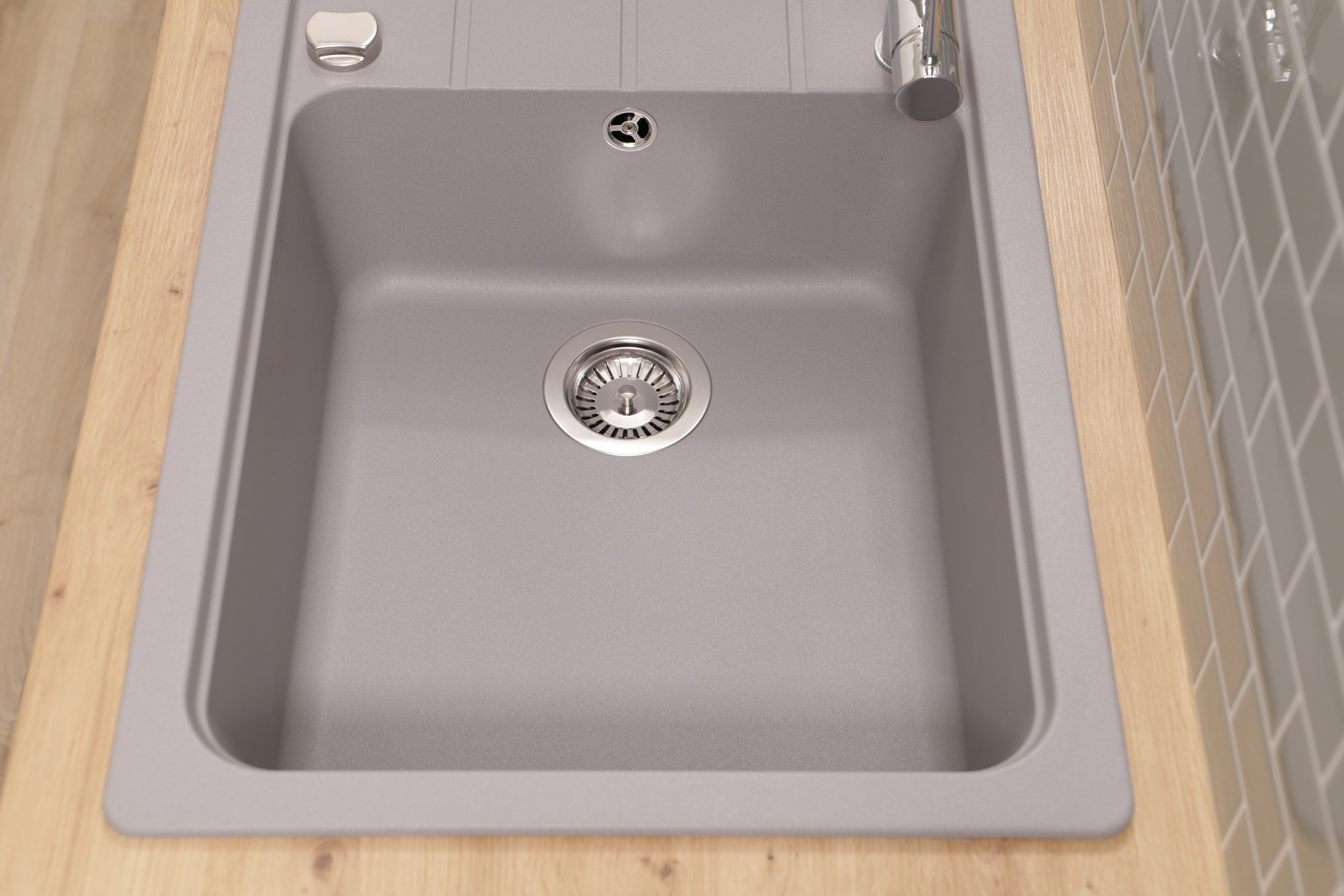 Eine Draufsicht auf ein graues Spülbecken mit silbernem Wasserhahn, Abfluss und hölzerner Arbeitsplatte.