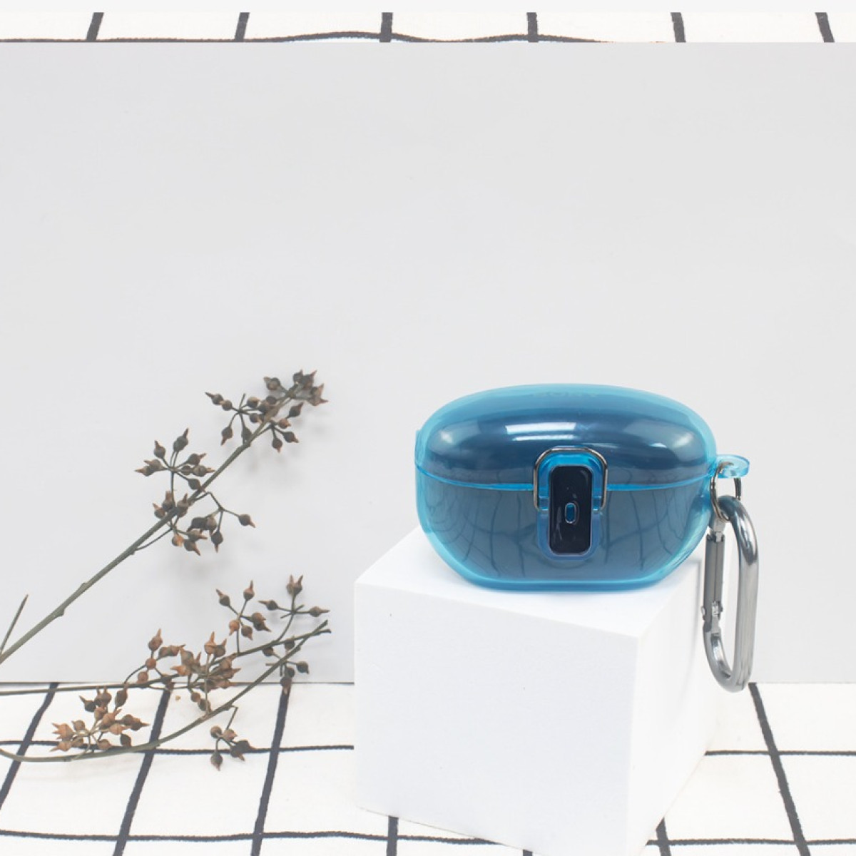 Blaues Ohrhörer-Etui auf einem weißen Würfel mit einer Pflanze im Hintergrund.