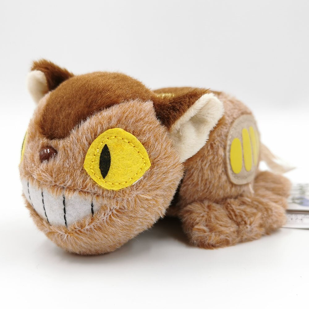 Ein braunes Plüschtier Katze mit gelben Augen und einem großen Lächeln, liegend auf weißer Oberfläche.