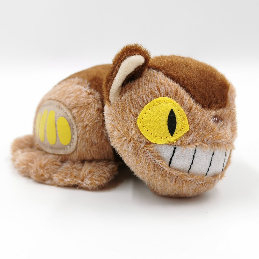 Ein braunes Plüschtier Katze mit gelben Augen und einem großen Lächeln, liegend auf weißer Oberfläche.