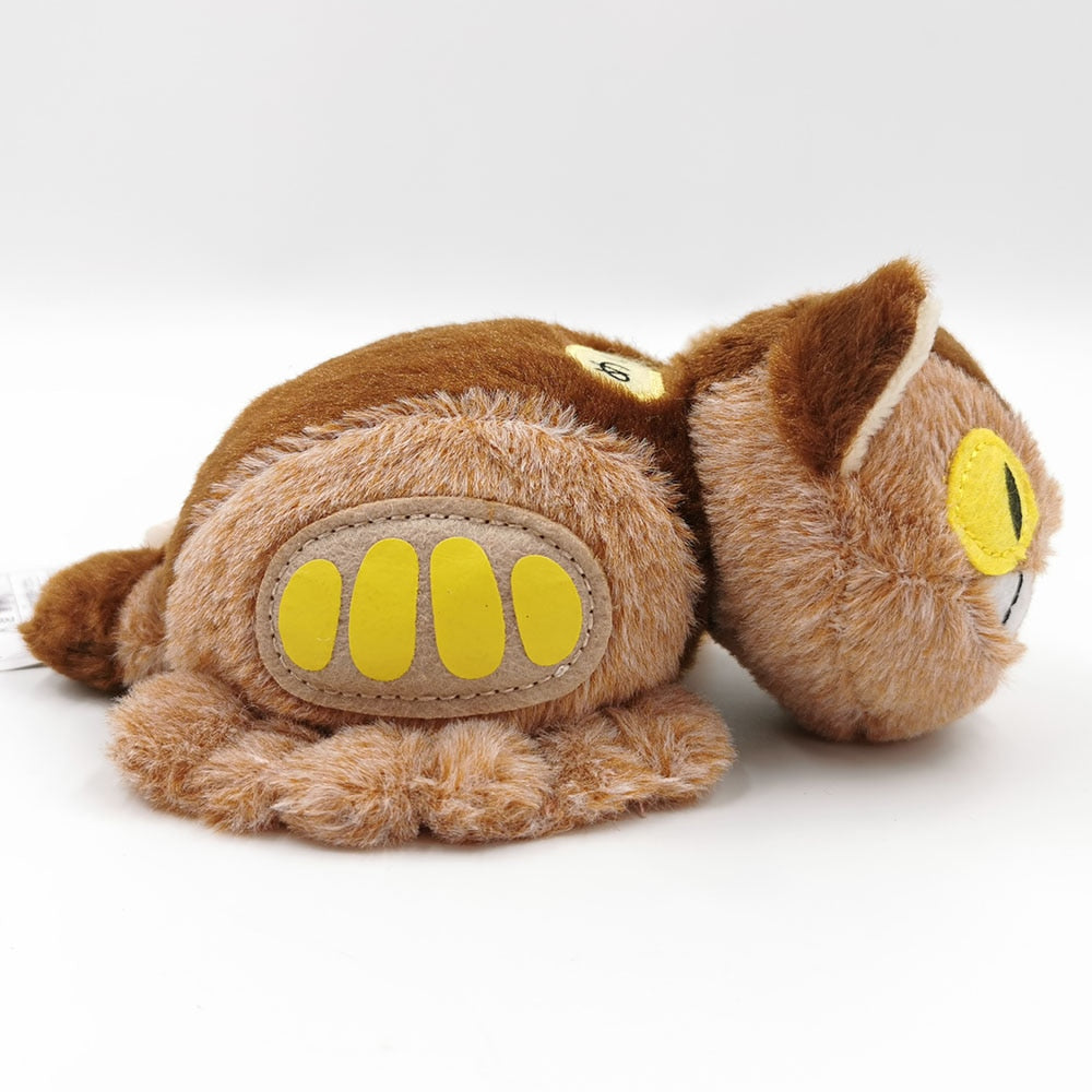 Ein braunes Plüschtier Katze mit gelben Akzenten, auf der Seite liegend auf weißer Oberfläche.