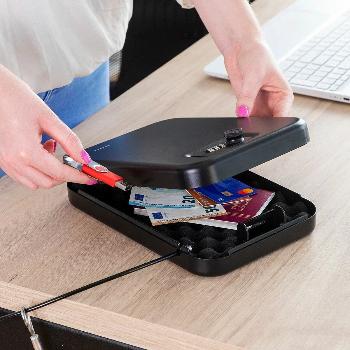 Una mano sta inserendo una USB in una cassaforte nera. Denaro, carte e un passaporto sono nella cassaforte.