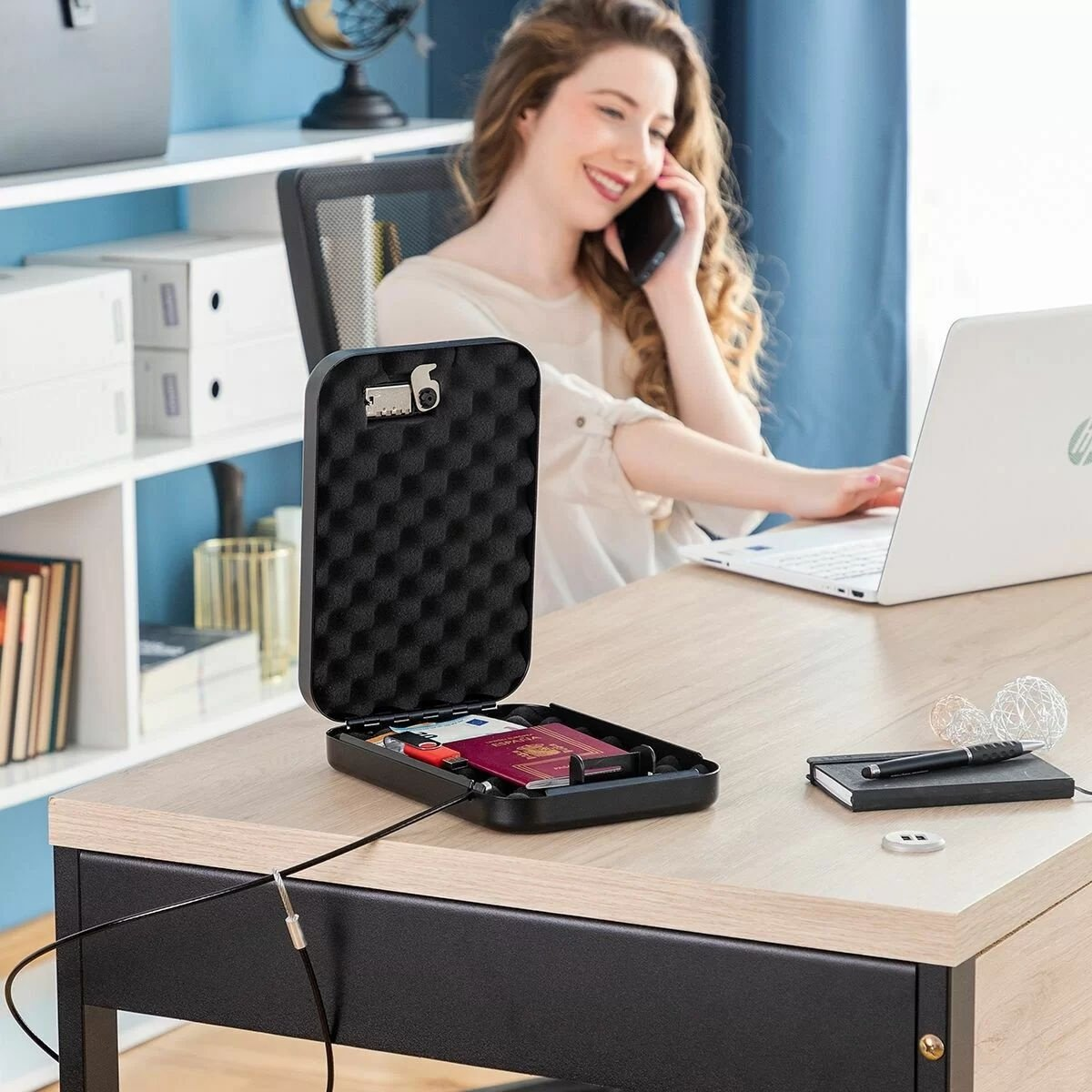 Donna alla scrivania con cassaforte, laptop e telefono. Cassaforte aperta, rivela oggetti.