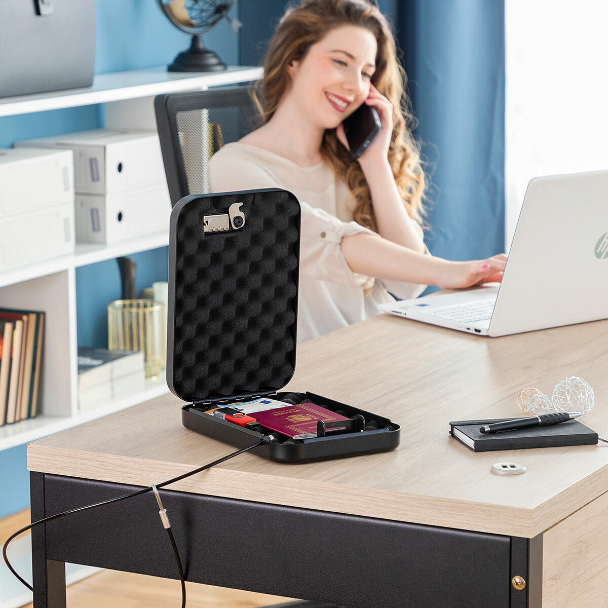 Donna alla scrivania con cassaforte, laptop e telefono. Cassaforte aperta, rivela oggetti.