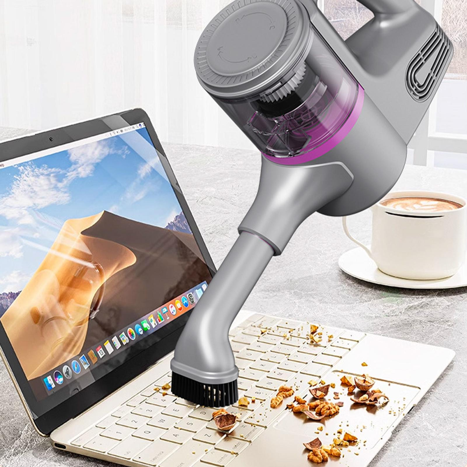 Ein grauer Staubsauger reinigt Krümel von einer Laptop-Tastatur, mit einer Tasse Kaffee im Hintergrund.