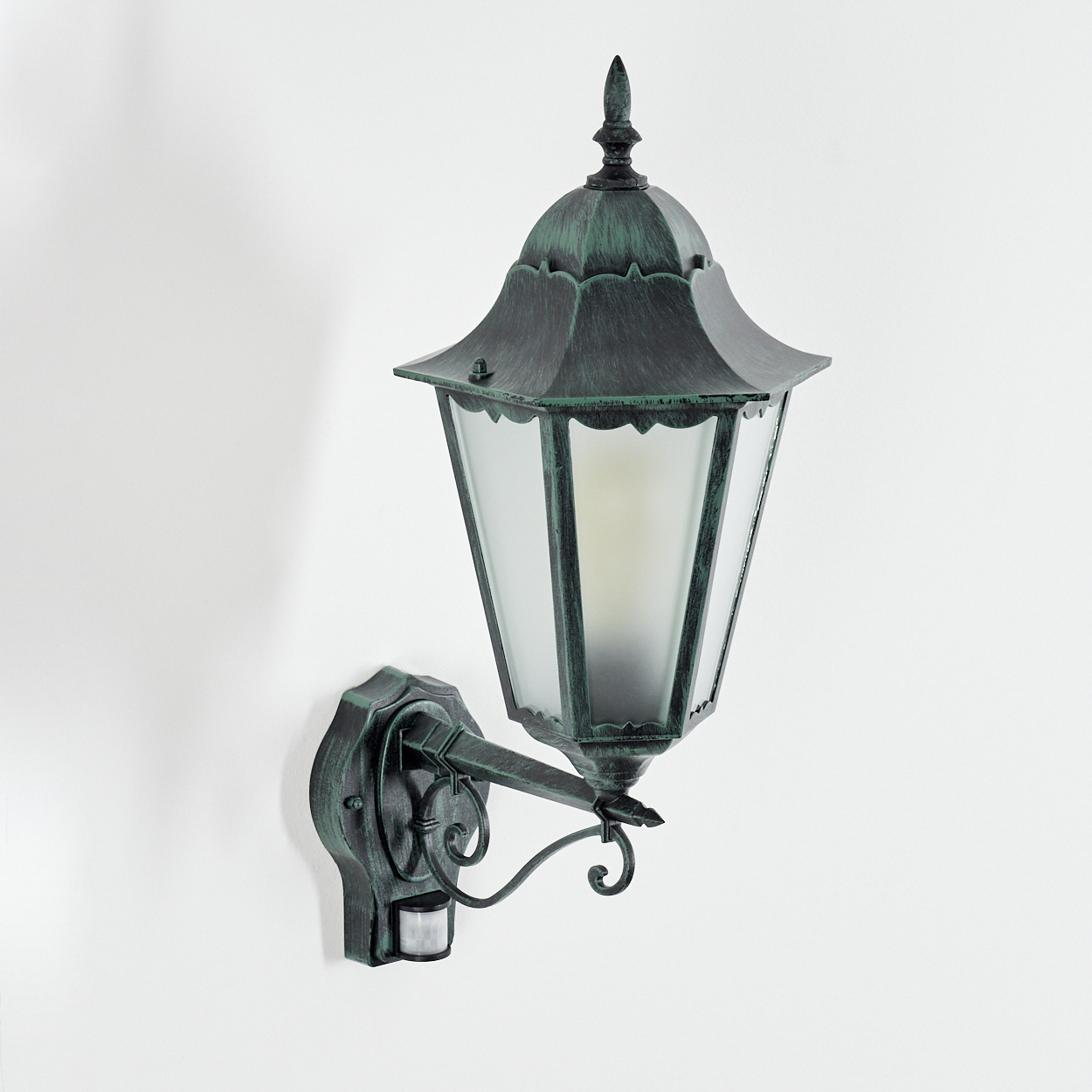 Außenlampe, grün mit weißem Wandhintergrund. Sie hat einen Bewegungssensor.