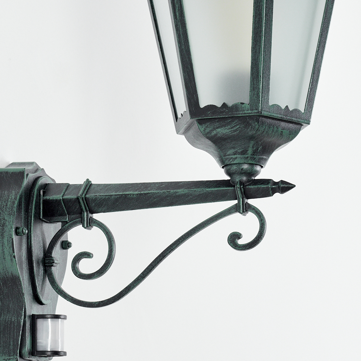 Außenlampe an einer weißen Wand montiert. Sie hat eine grünlich-bronzene Oberfläche und klares Glas.