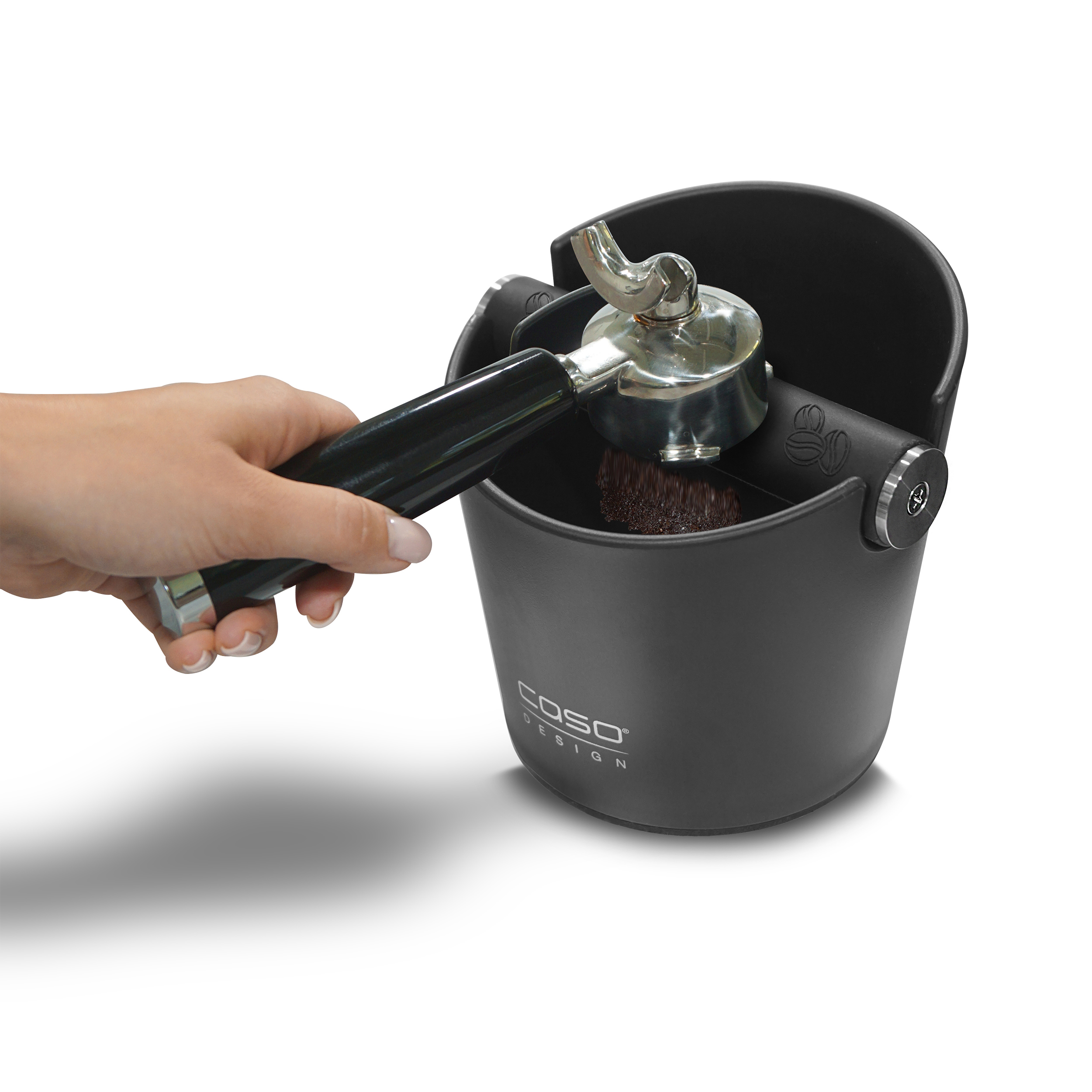 Eine Hand schlägt einen Siebträger gegen eine schwarze Abschlagbox, um Espressosatz zu entfernen.