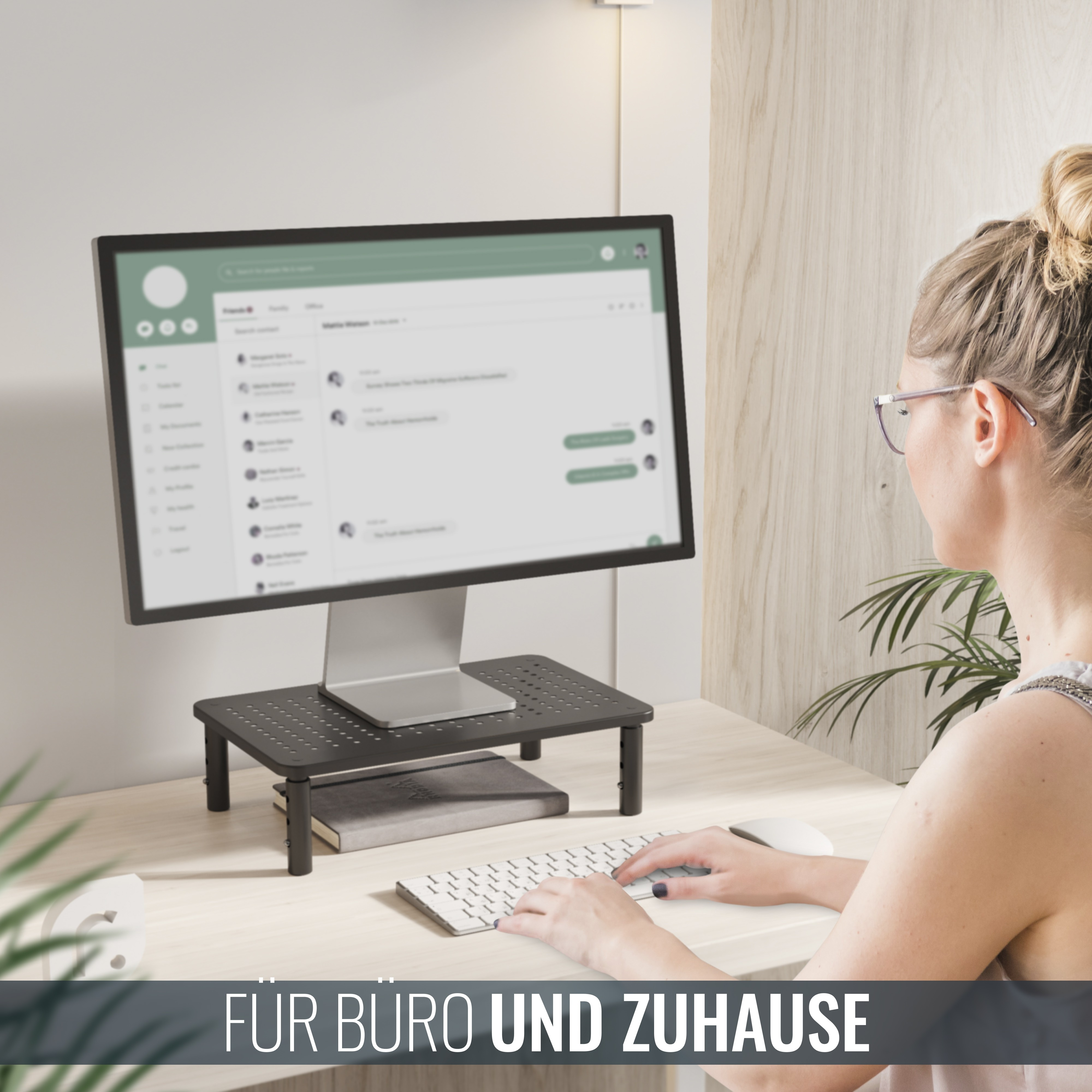 Ein Monitor steht auf einem schwarzen, verstellbaren Ständer auf einem Schreibtisch mit Tastatur, Maus und einer Frau, die den Computer benutzt.