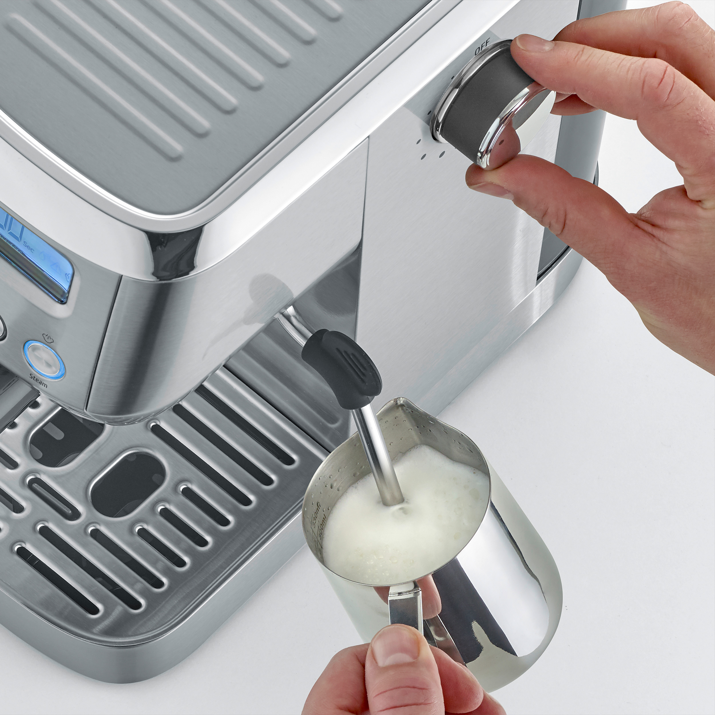 Eine Hand schäumt Milch mit einer silbernen Espressomaschine auf.