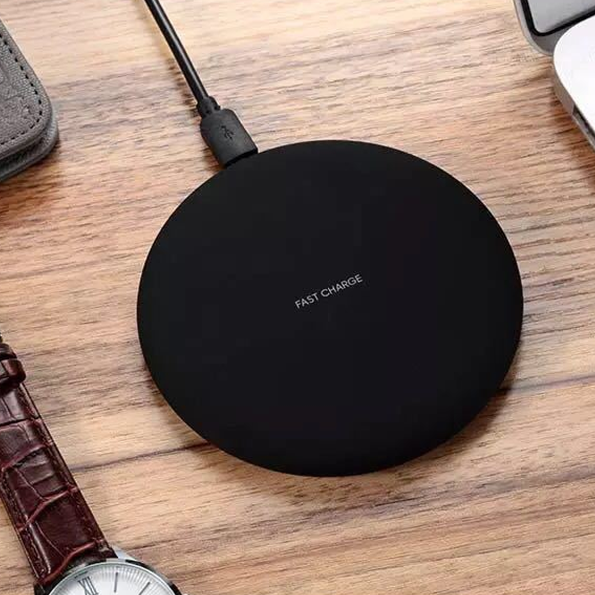 Ein schwarzes kabelloses Ladepad mit dem Text „FAST CHARGE“ auf einem Holztisch.