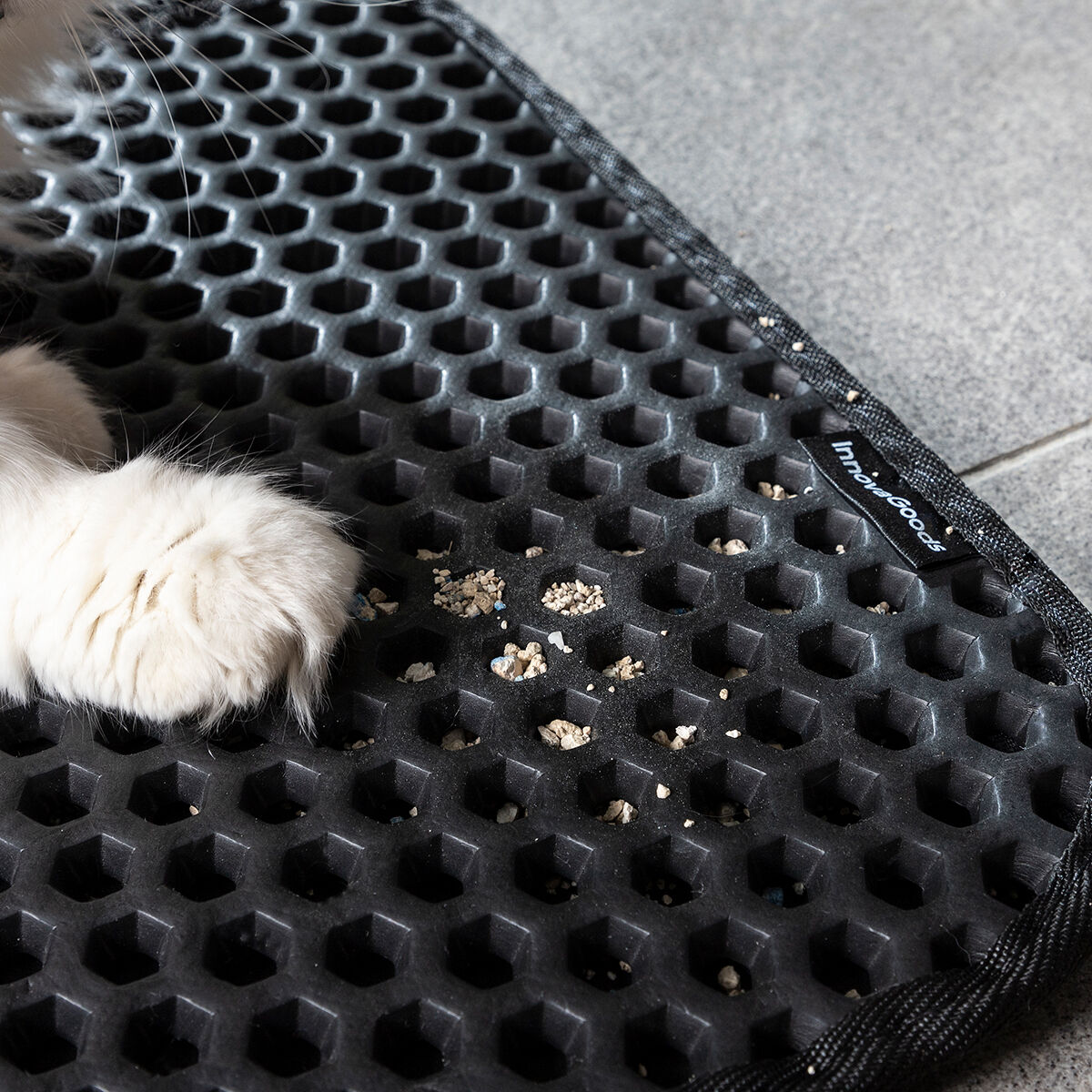 Primer plano de la pata de un gato sobre una alfombra negra de panal con arena dispersa.