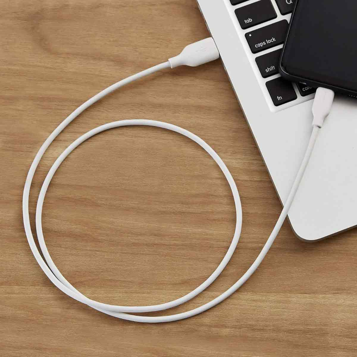 Ein weißes Ladekabel verbindet ein schwarzes Smartphone mit einem silbernen Laptop auf einer Holzoberfläche.