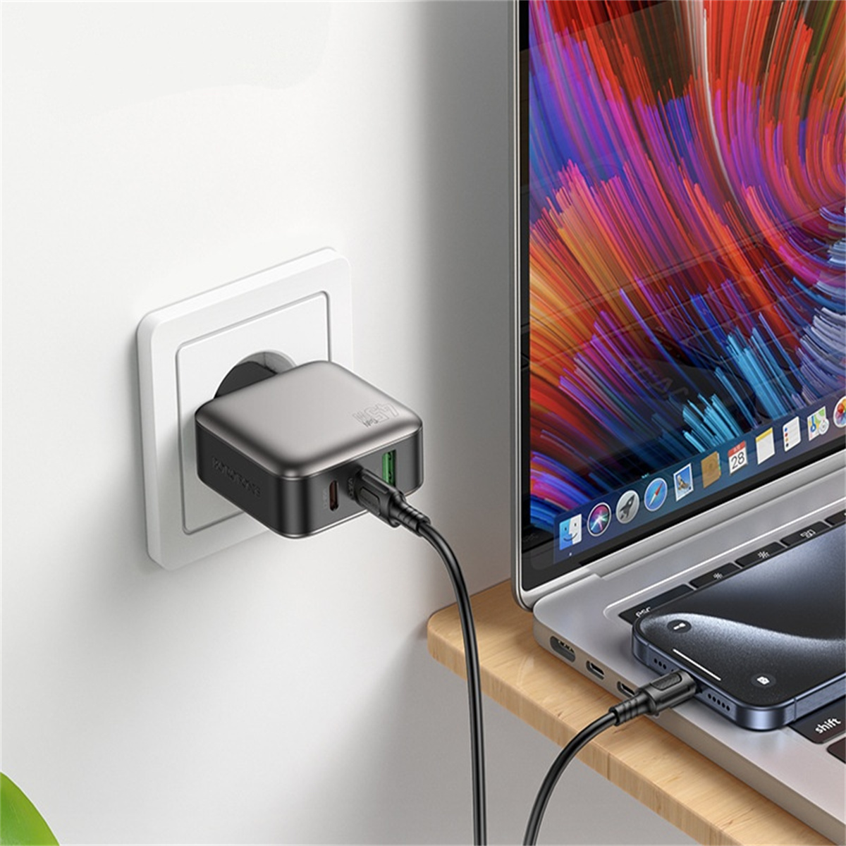 Graues USB-Ladegerät an einer Wand angeschlossen, mit einem Laptop und einem aufladenden Telefon.