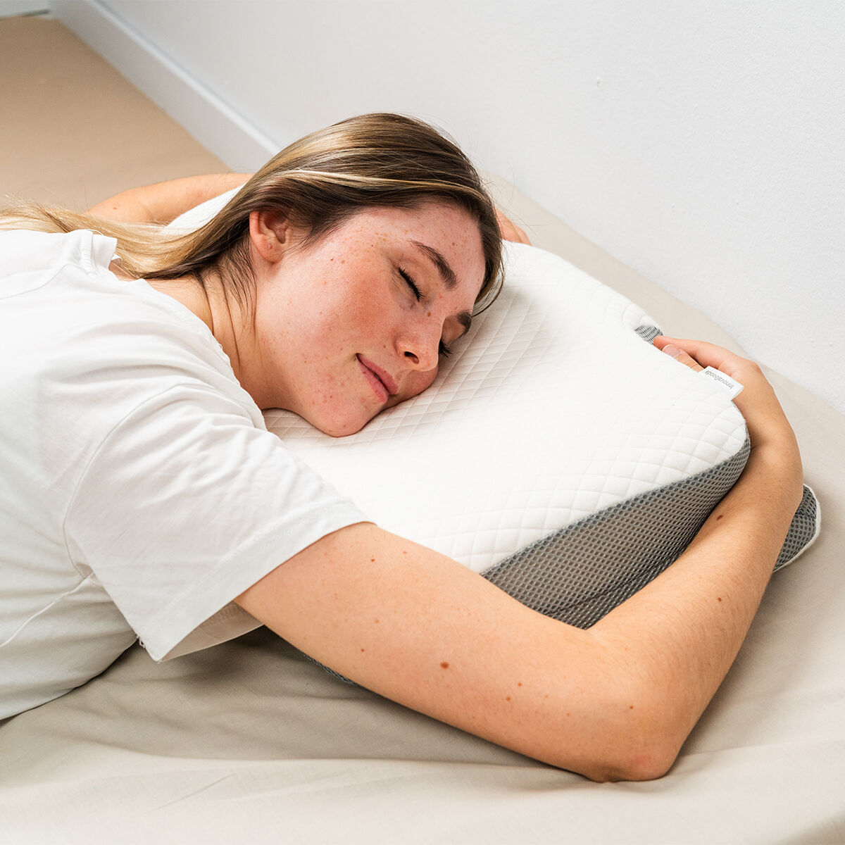 Frau schläft auf einem weißen und grauen orthopädischen Kissen.