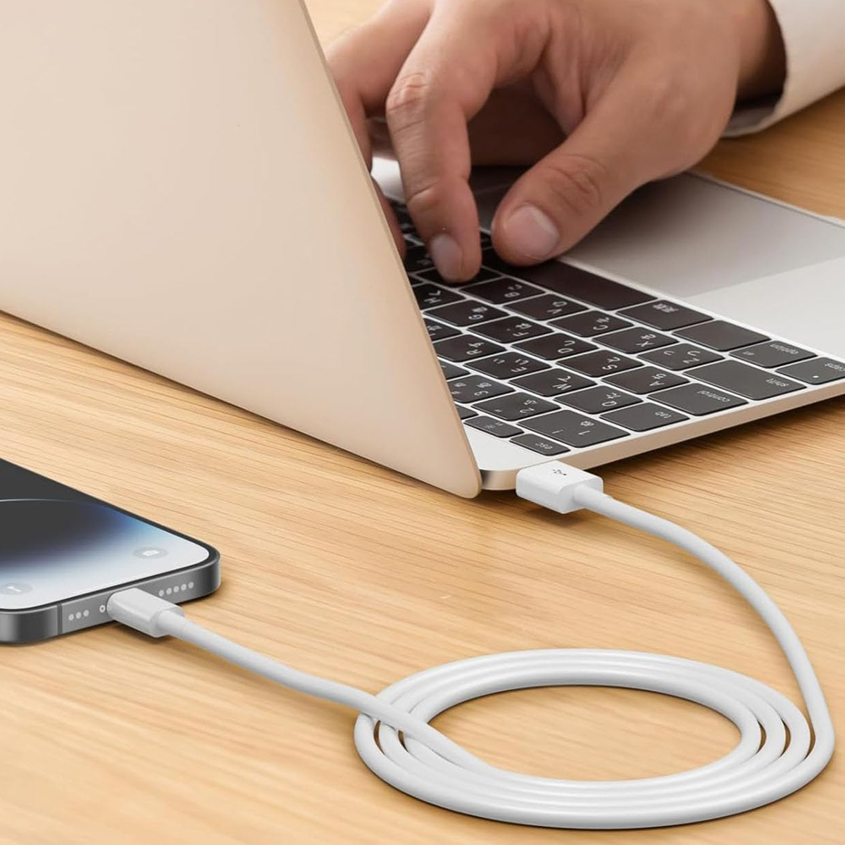 Ein Telefon und ein Laptop sind mit einem weißen Ladekabel auf einer Holzoberfläche verbunden.