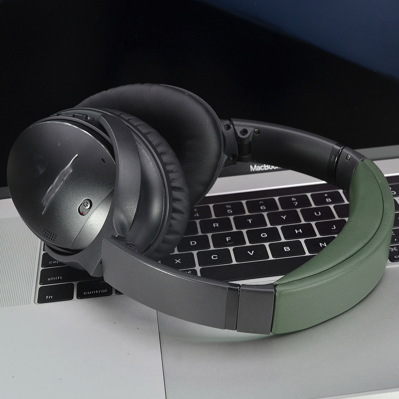 Een grijze en zwarte hoofdtelefoonset met een olijfgroene hoofdband op een laptoptoetsenbord.