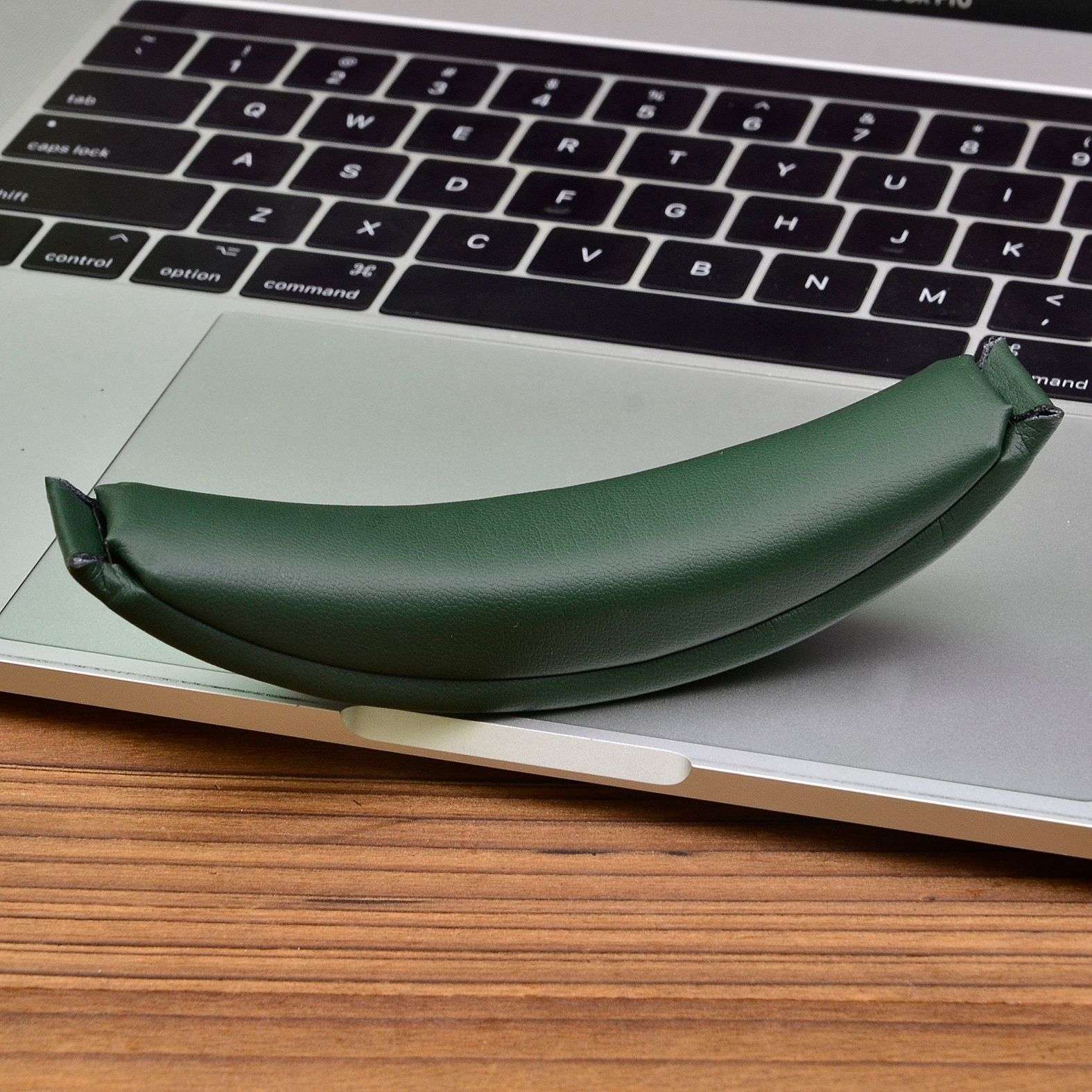 Groene hoofdtelefoonband rustend op een zilveren laptop op een houten bureau.