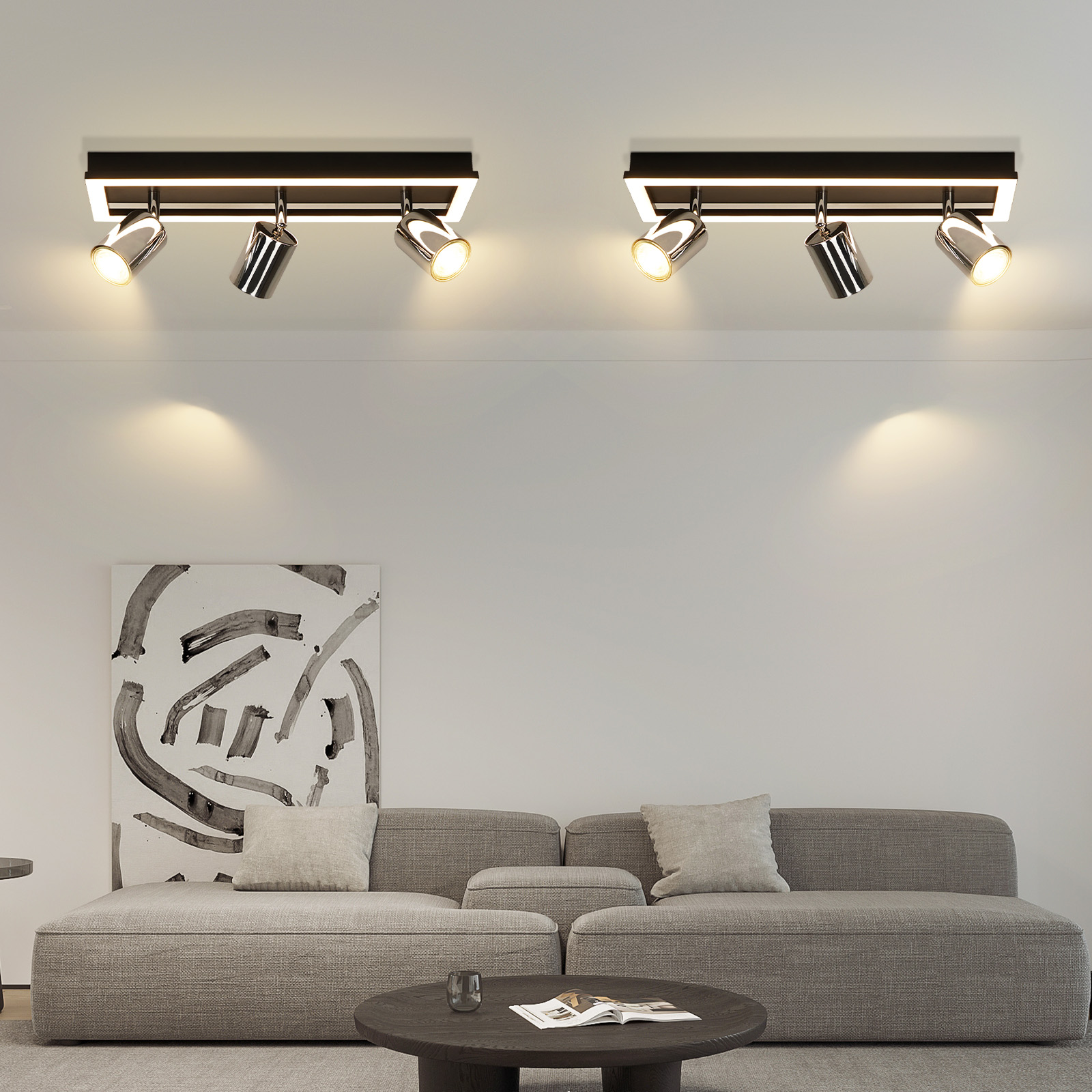 L'immagine mostra un soggiorno con due faretti a soffitto, un divano grigio e un dipinto astratto sulla parete.