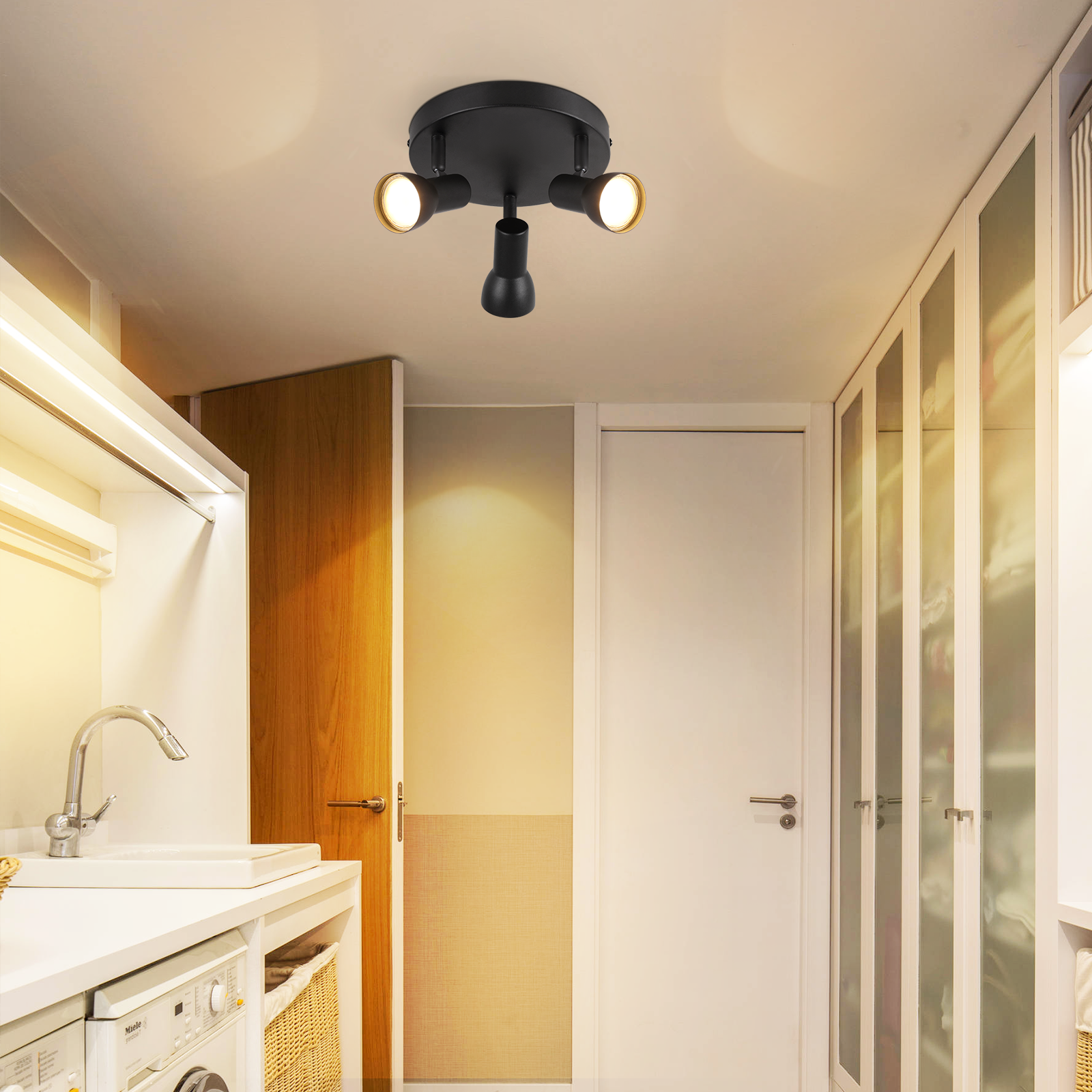 Czarna oprawa oświetleniowa sufitowa z trzema podświetlonymi reflektorami. W pralni z pralką.