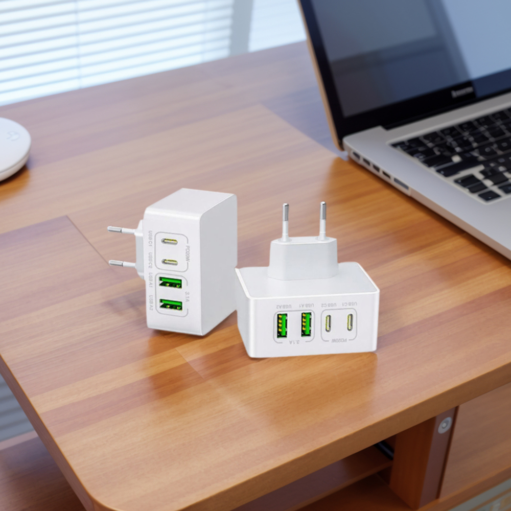 Zwei weiße USB-Ladegeräte auf einem Holztisch, mit einem Laptop im Hintergrund.