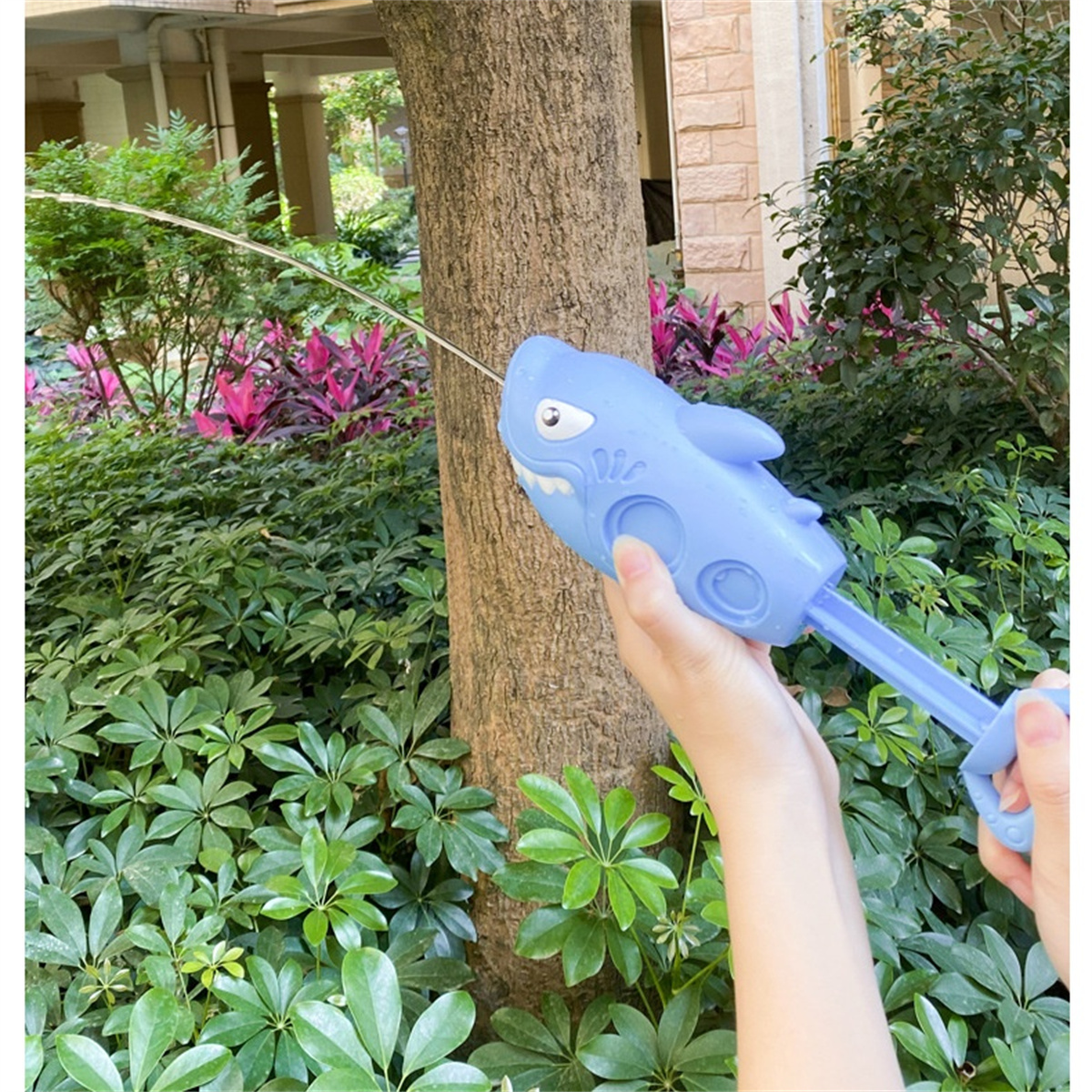 Eine blaue Hai-Wasserpistole schießt Wasser in einer Gartenumgebung.
