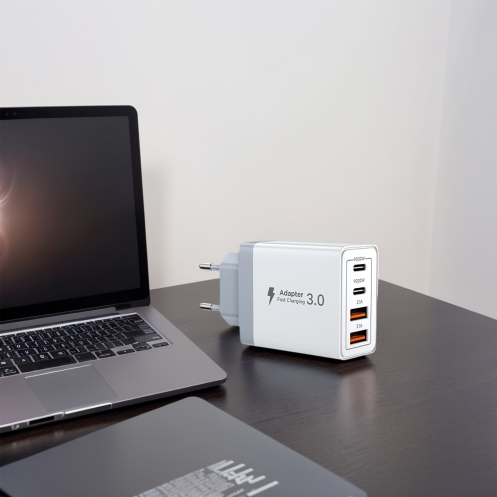 Weißes USB-Ladegerät mit mehreren Anschlüssen und grauem Adapter neben einem Laptop.