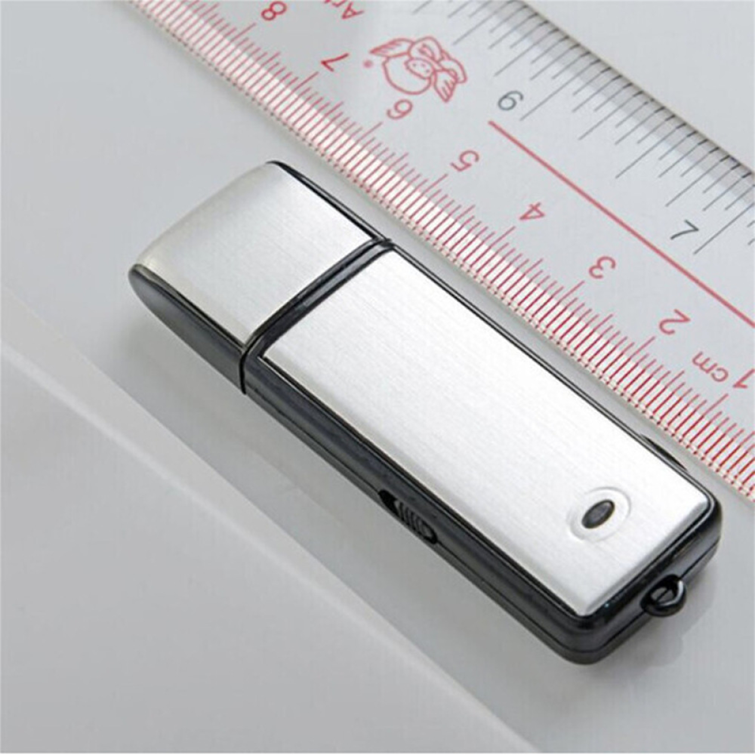 Silberner und schwarzer USB-Stick mit einem Lineal im Hintergrund, isoliert auf einer weißen Oberfläche.