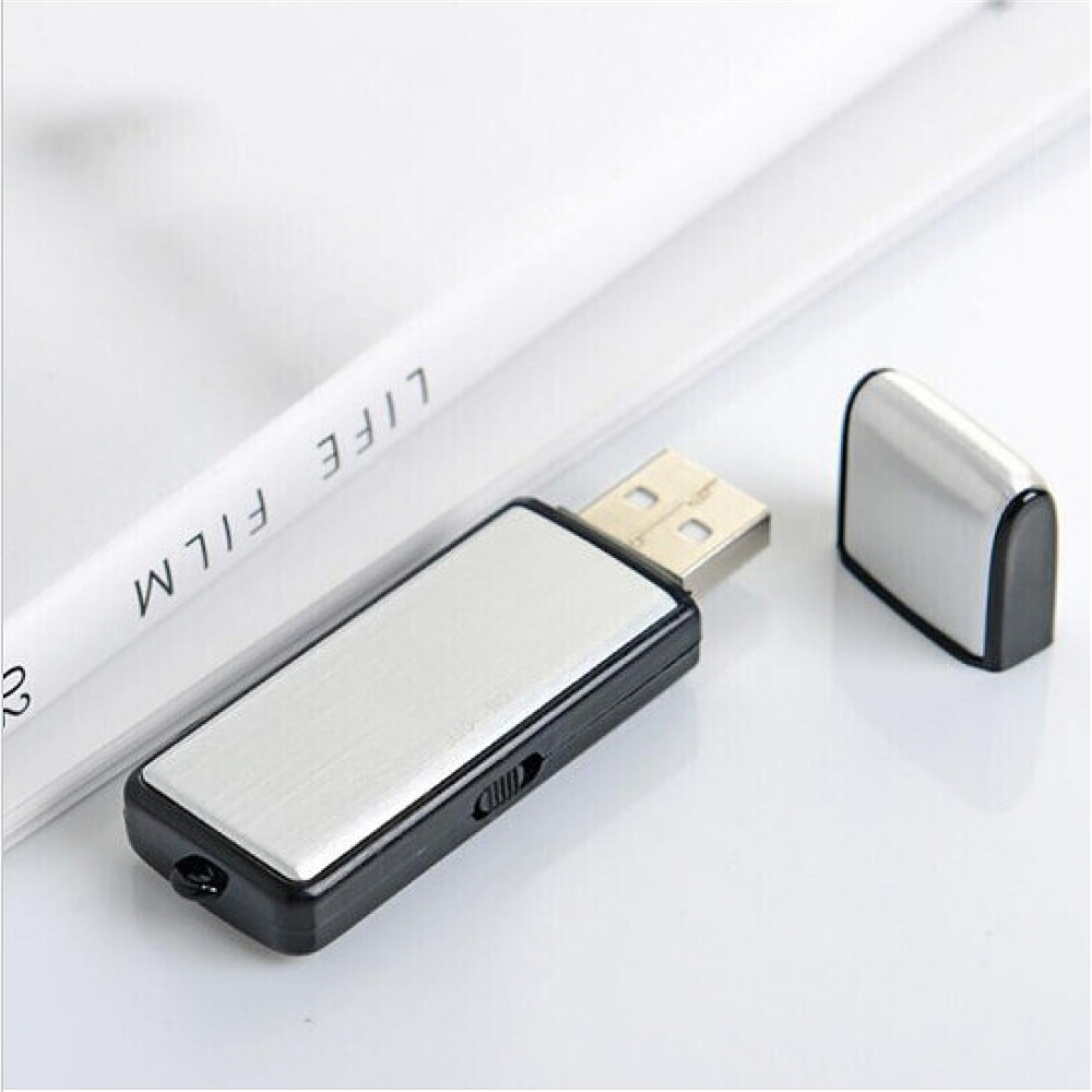 Ein silberner und schwarzer USB-Stick mit abgenommener Kappe, der auf einer weißen Oberfläche neben einer Zeitschrift liegt.