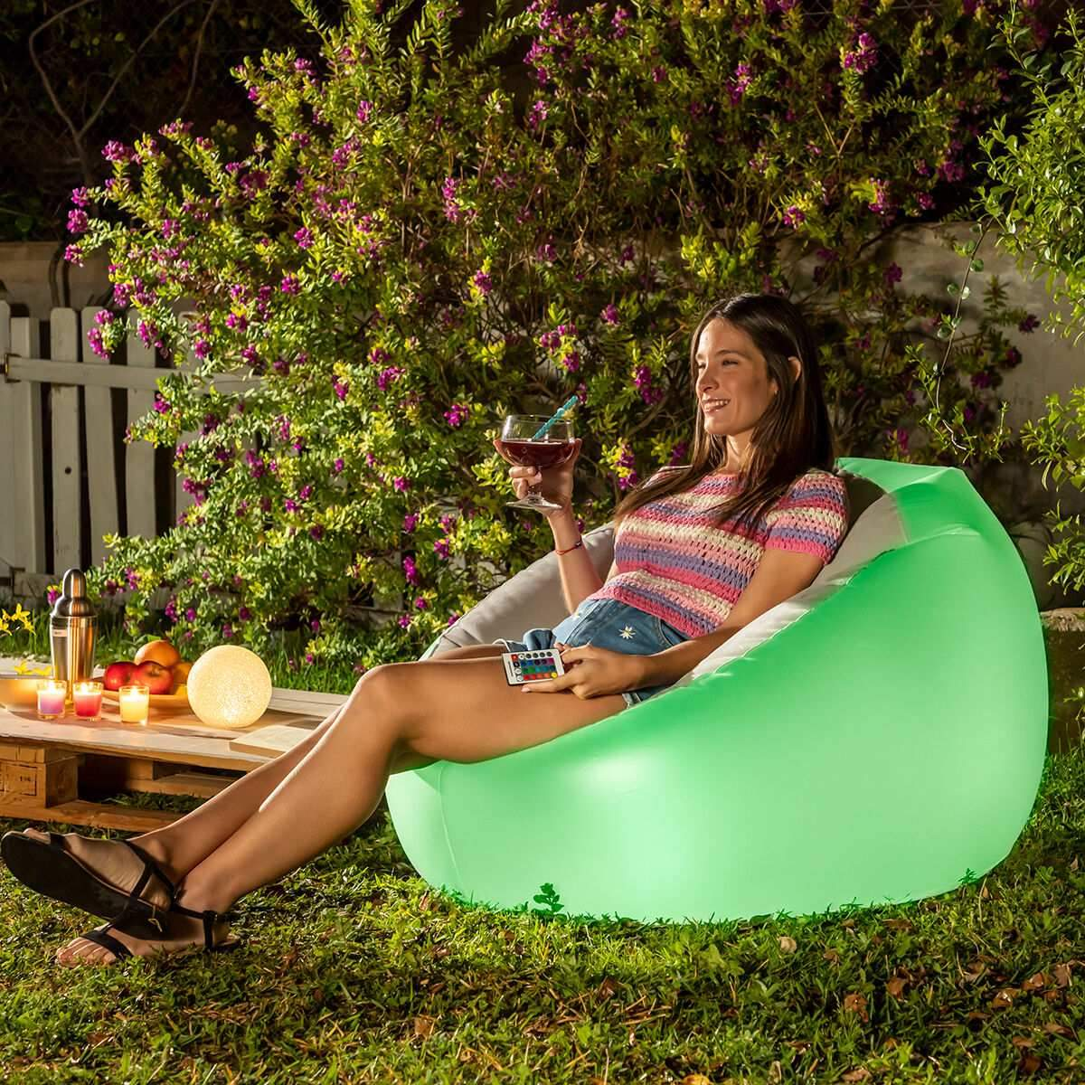 Donna che si rilassa su una sedia gonfiabile verde in un giardino di notte, con un drink in mano.
