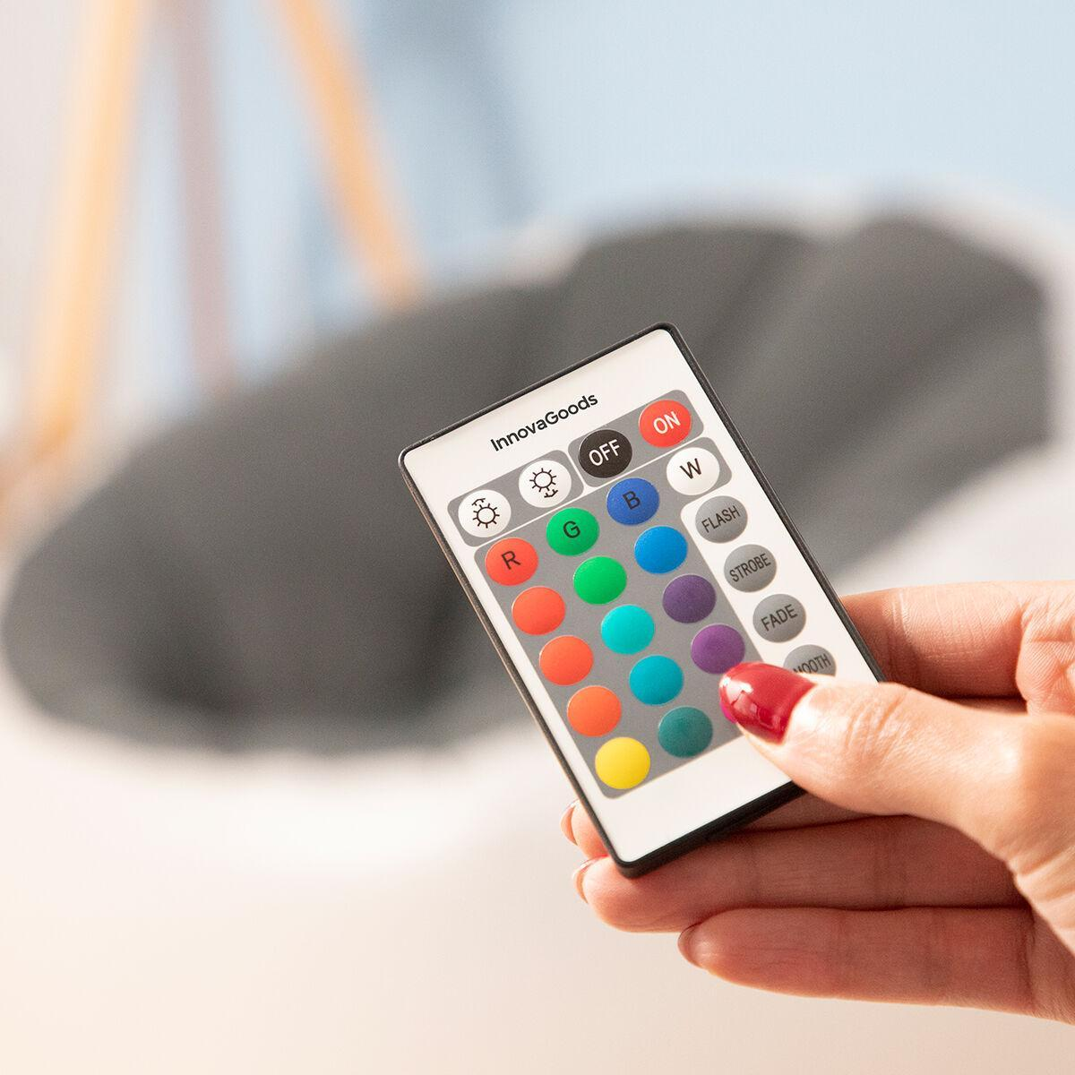 Una mano tiene in mano un telecomando con pulsanti colorati, che controlla una luce LED, con un oggetto grigio sfocato sullo sfondo.