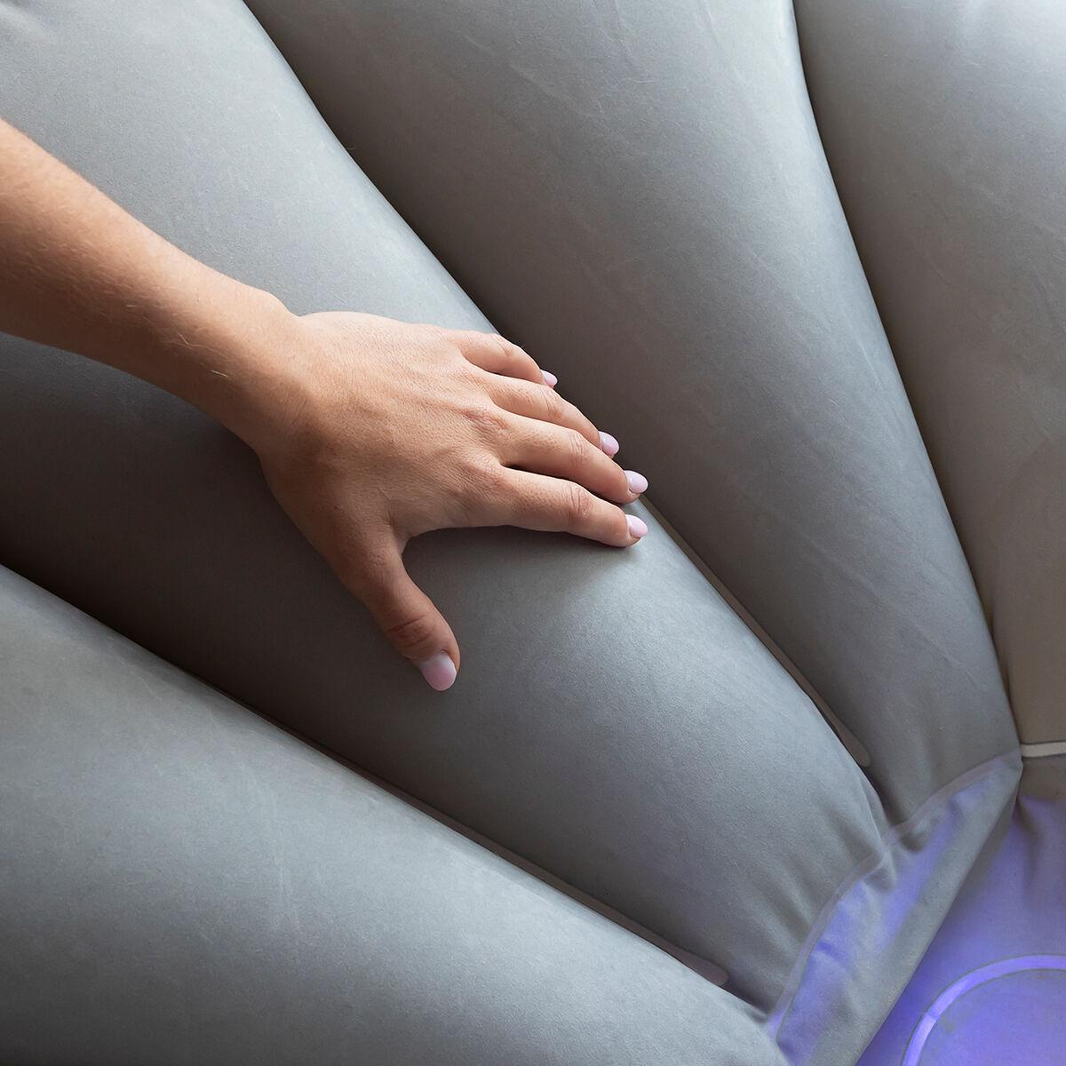 Una mano poggia su un cuscino grigio a forma di conchiglia con luce che emana dal basso, catturata in un primo piano.