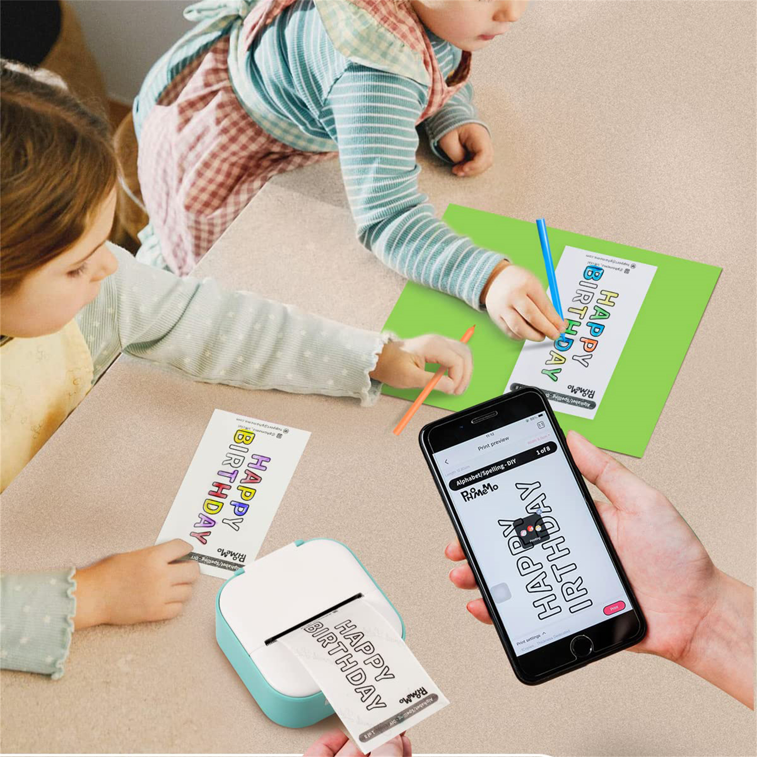 Kinder drucken mit einem blau-weißen Drucker "Happy Birthday"-Karten, wobei ein Telefon Druckvorschau anzeigt.