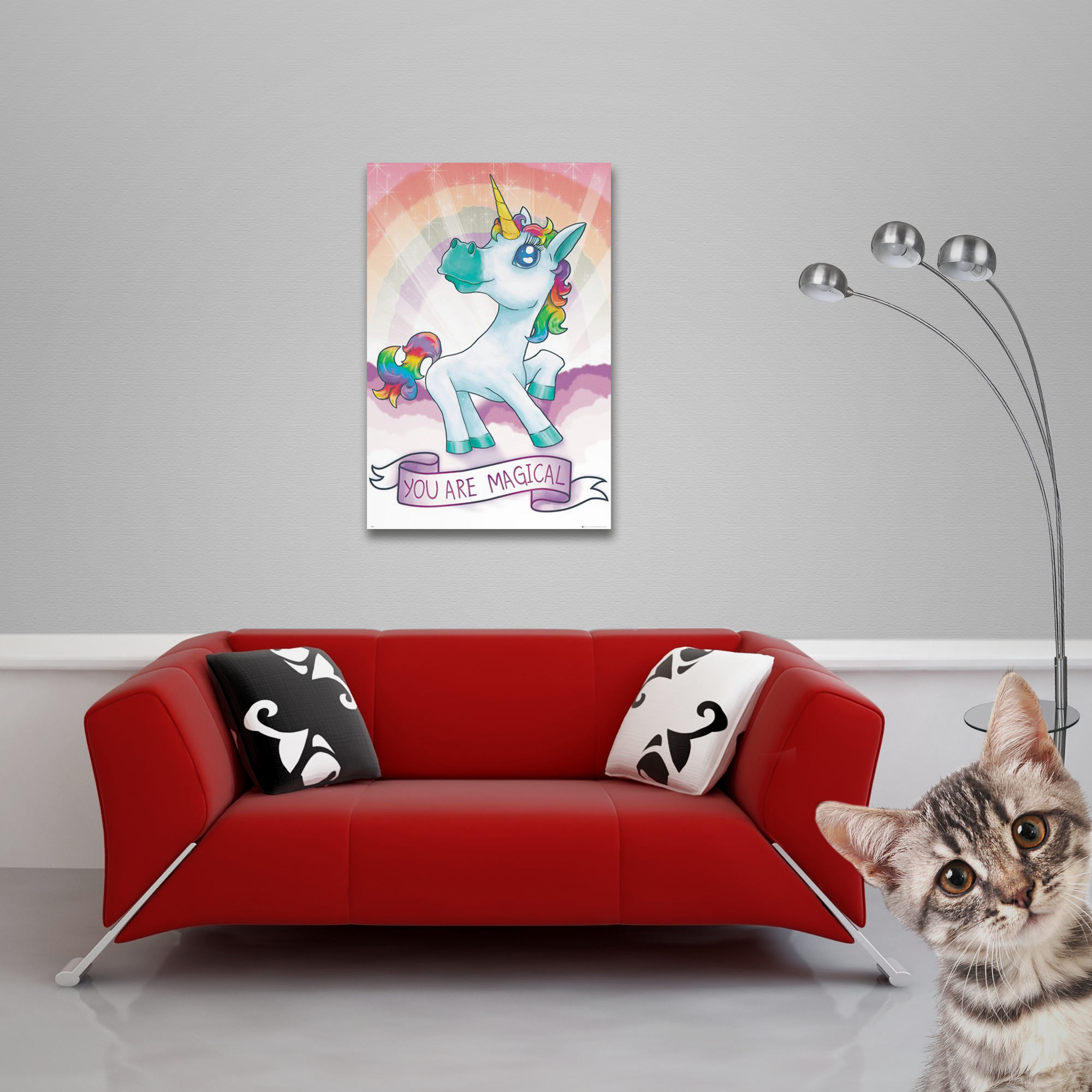 Ein Wohnzimmer mit einem roten Sofa und einem Einhornposter darüber, eine Katze in der unteren rechten Ecke.