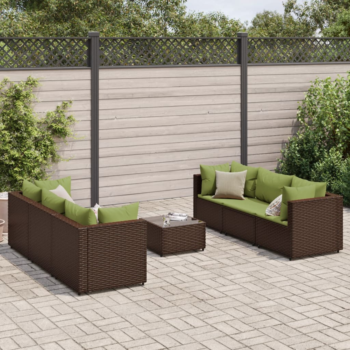Eine dunkelbraune Rattan-Terrassengarnitur mit grünen Kissen auf einer Steinterrasse mit Holzzaun.