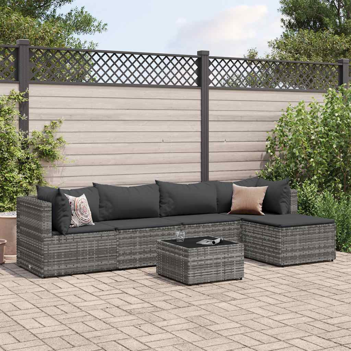 Un set da salotto sezionale da giardino in vimini grigio con cuscini e un tavolo su un patio in mattoni, con una recinzione dietro.